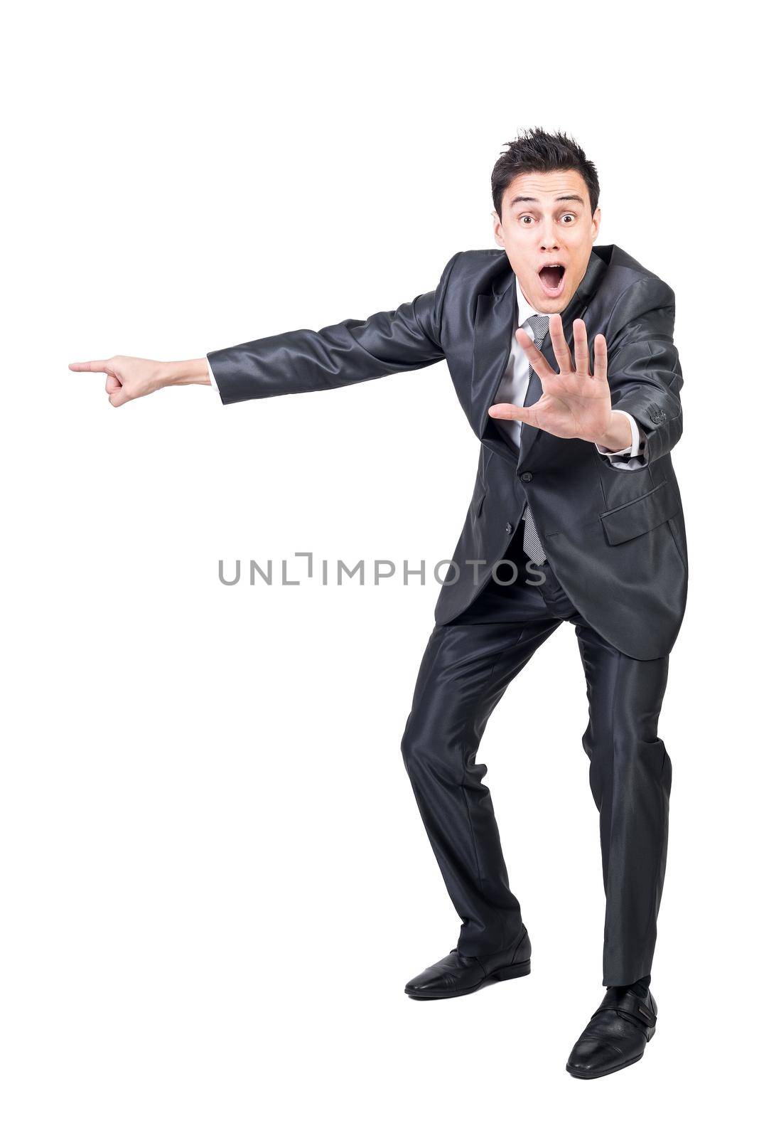 Full body of amazed male in formal suit pointing aside with outstretched arm and looking at camera with opened mouth isolated on white background