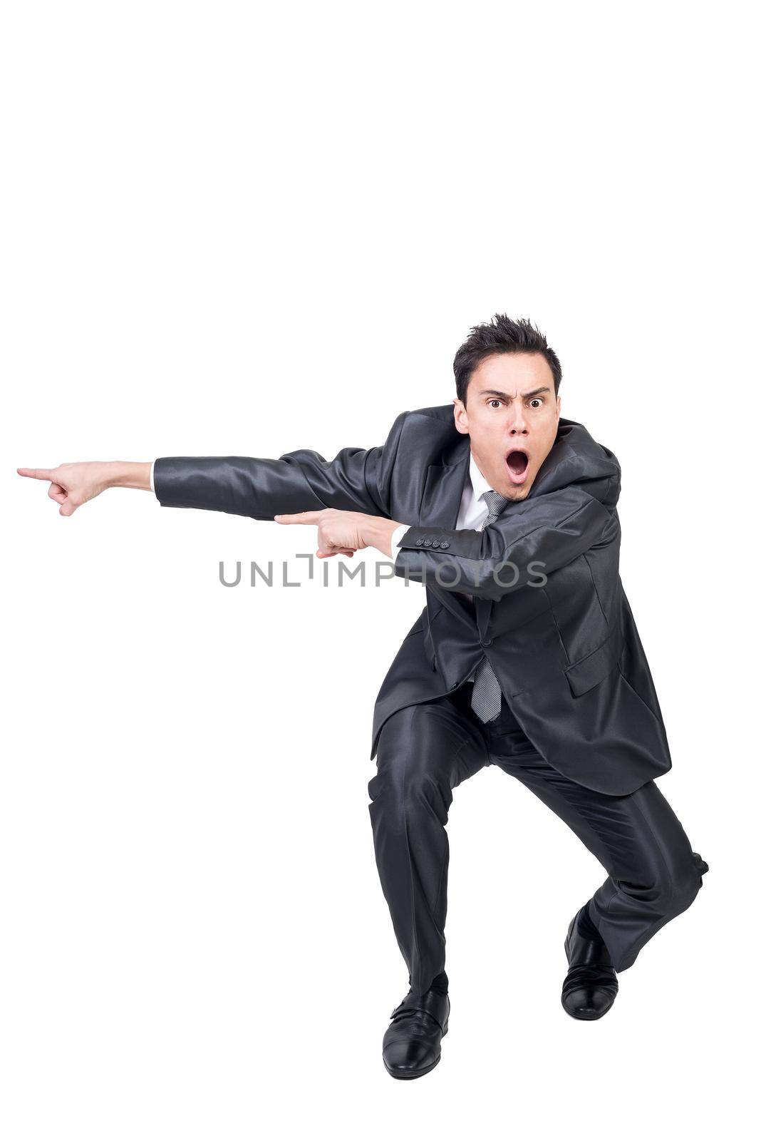 Full body of speechless man in formal suit hunkering down and pointing aside while looking at camera with astonished face isolated on white background