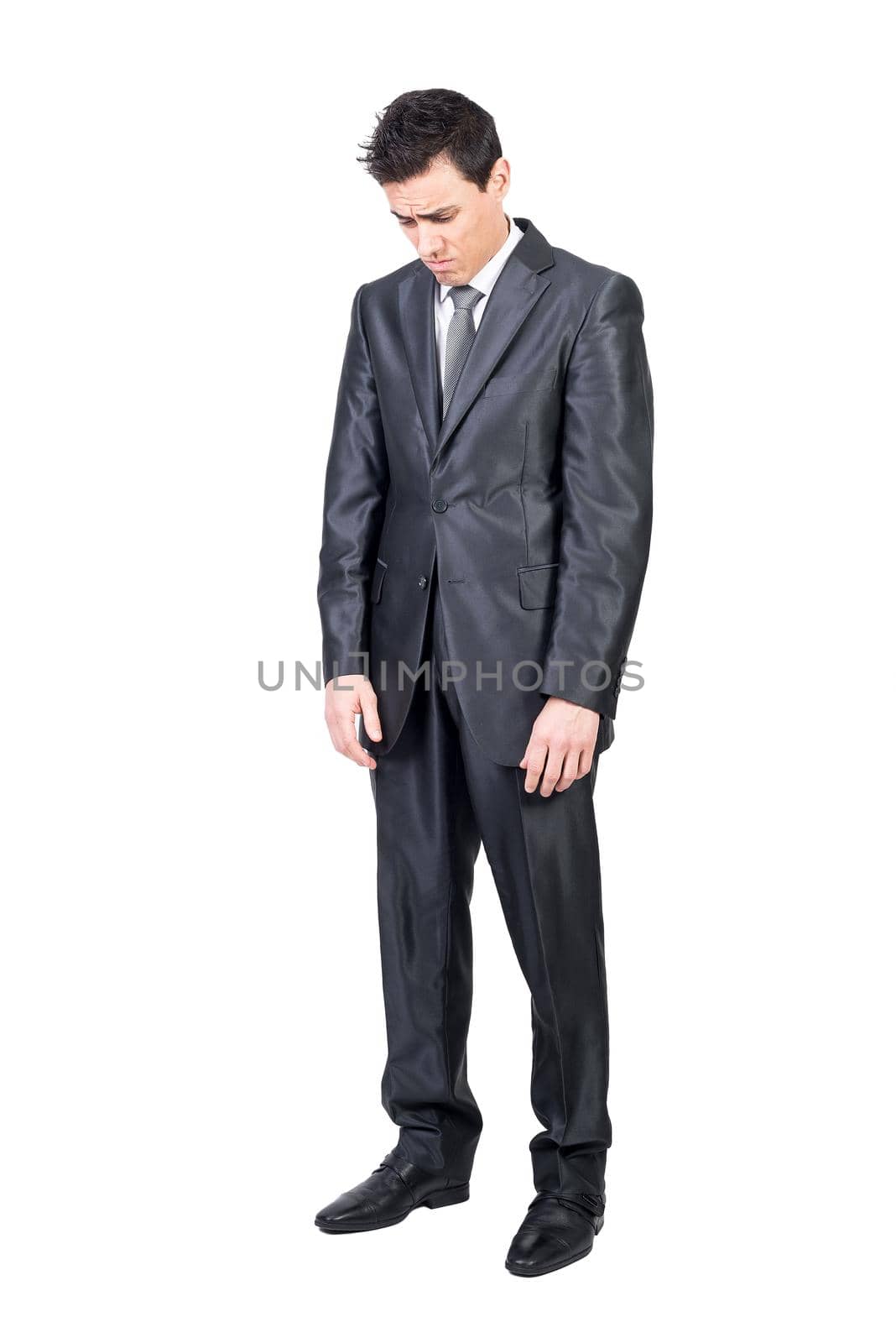 Full length of melancholic young male entrepreneur with dark hair in formal gray suit and tie looking away pensively while standing isolated on white background