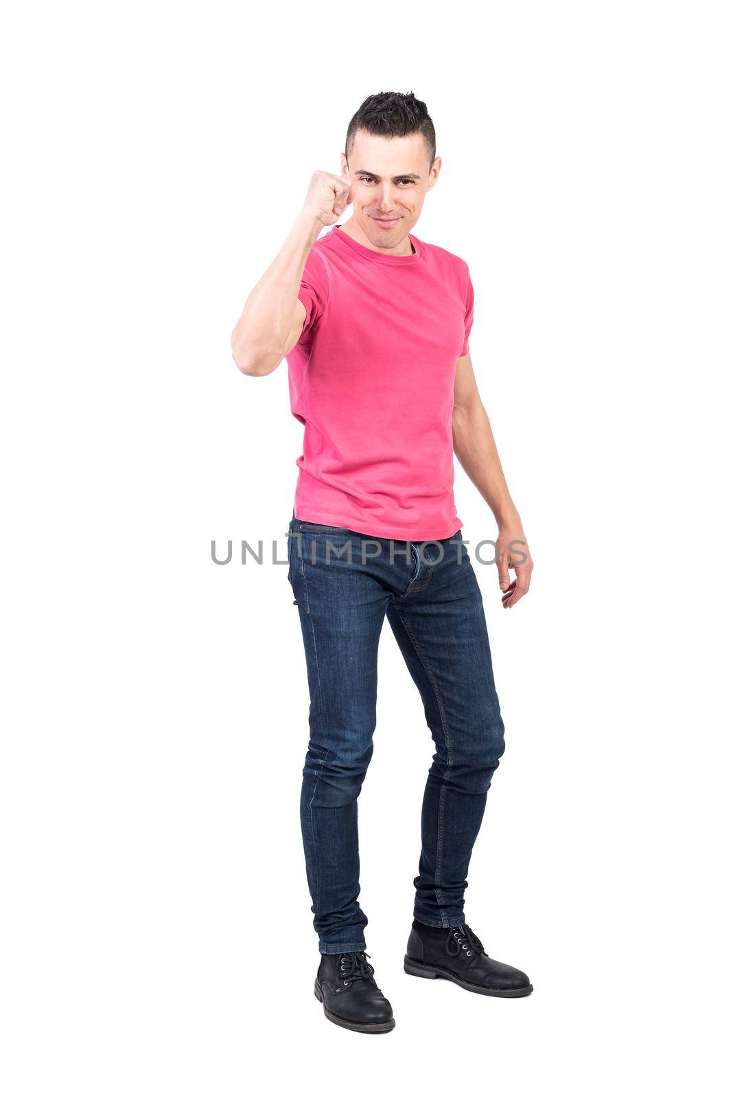 Full body confident male in jeans and pink t shirt looking at camera and clenching fist as sign of success against white background
