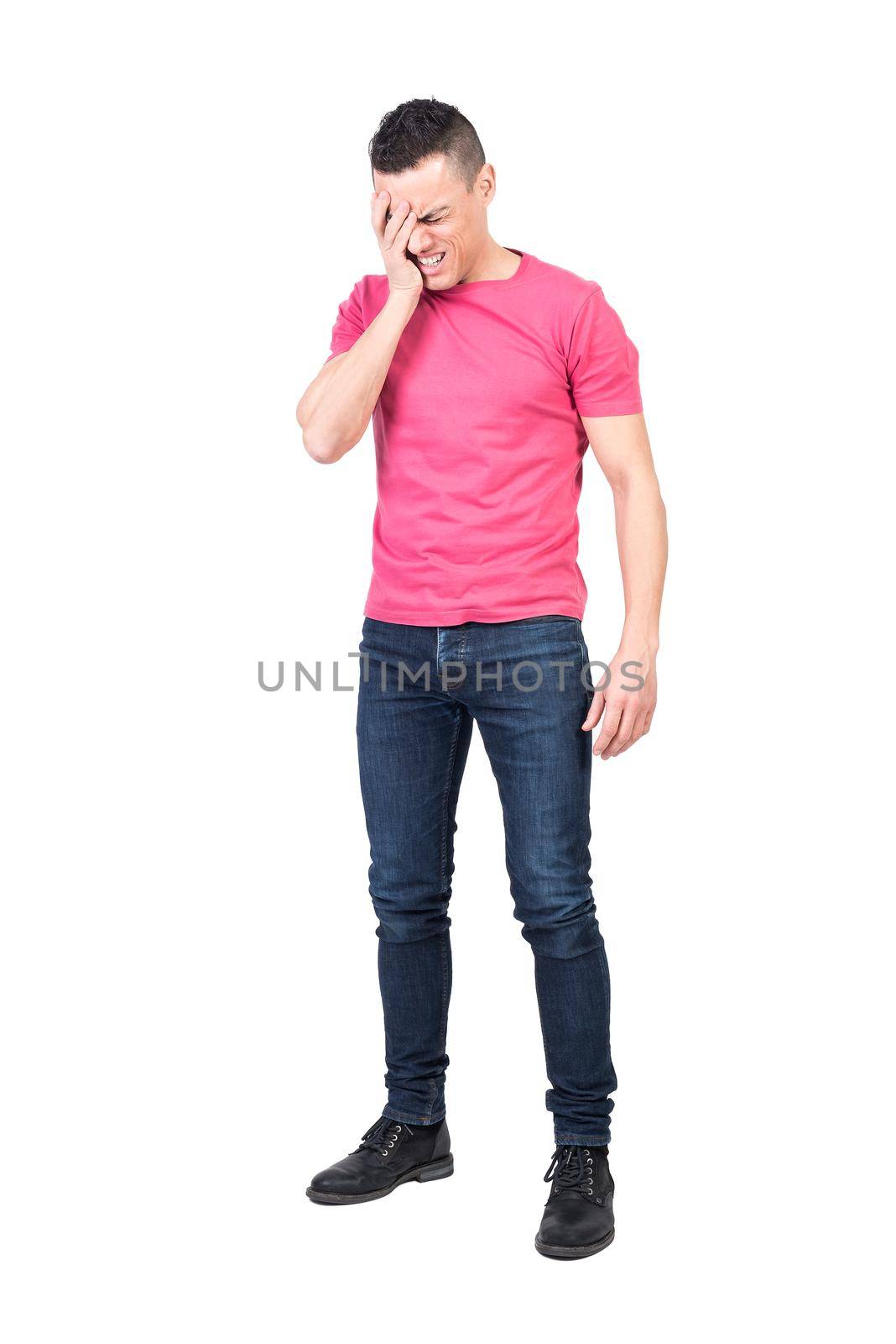Full length male in jeans and pink t shirt touching head and wincing while suffering from migraine against white background