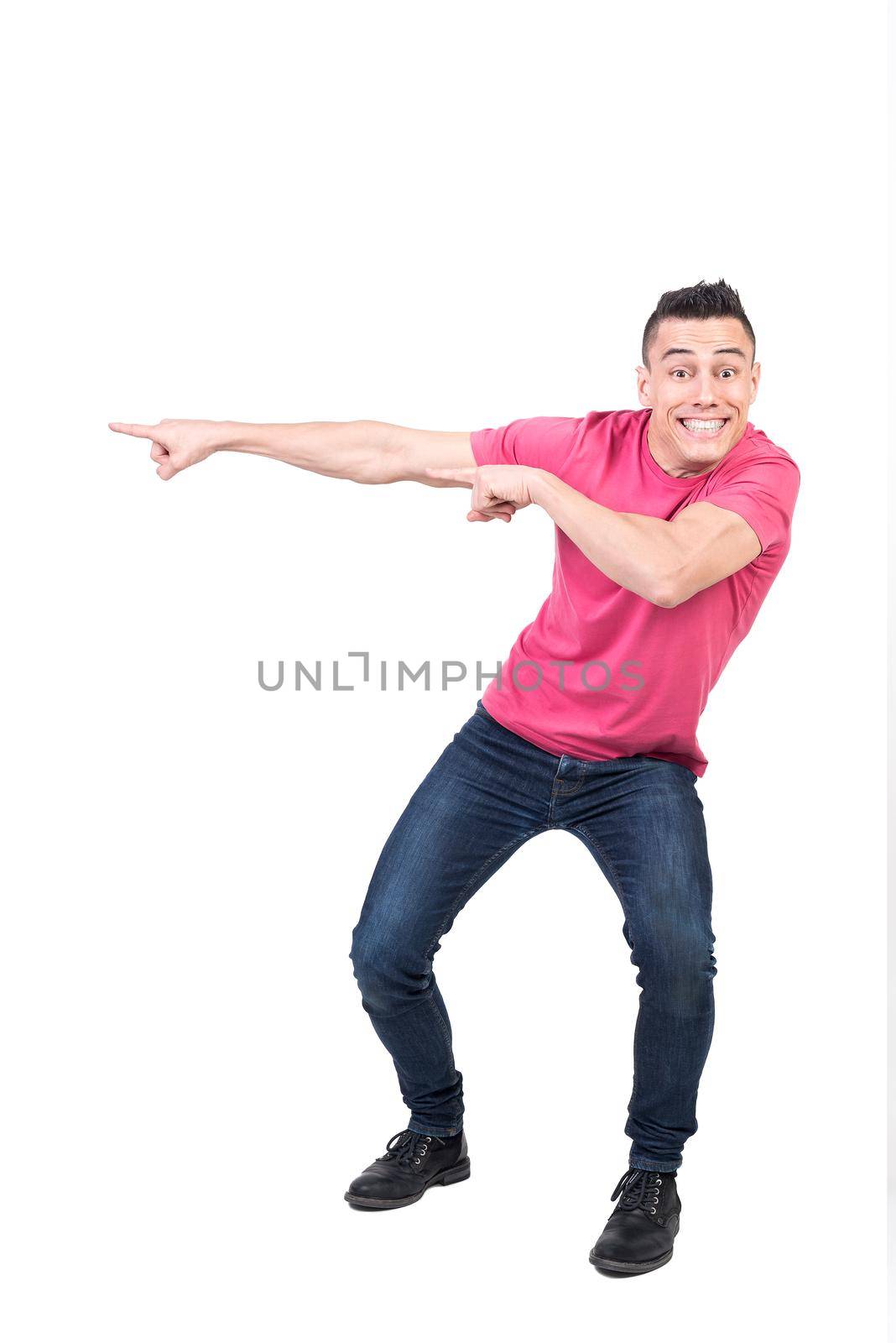 Full body of joyful male model pointing aside and looking at camera with toothy smile while standing isolated on white background