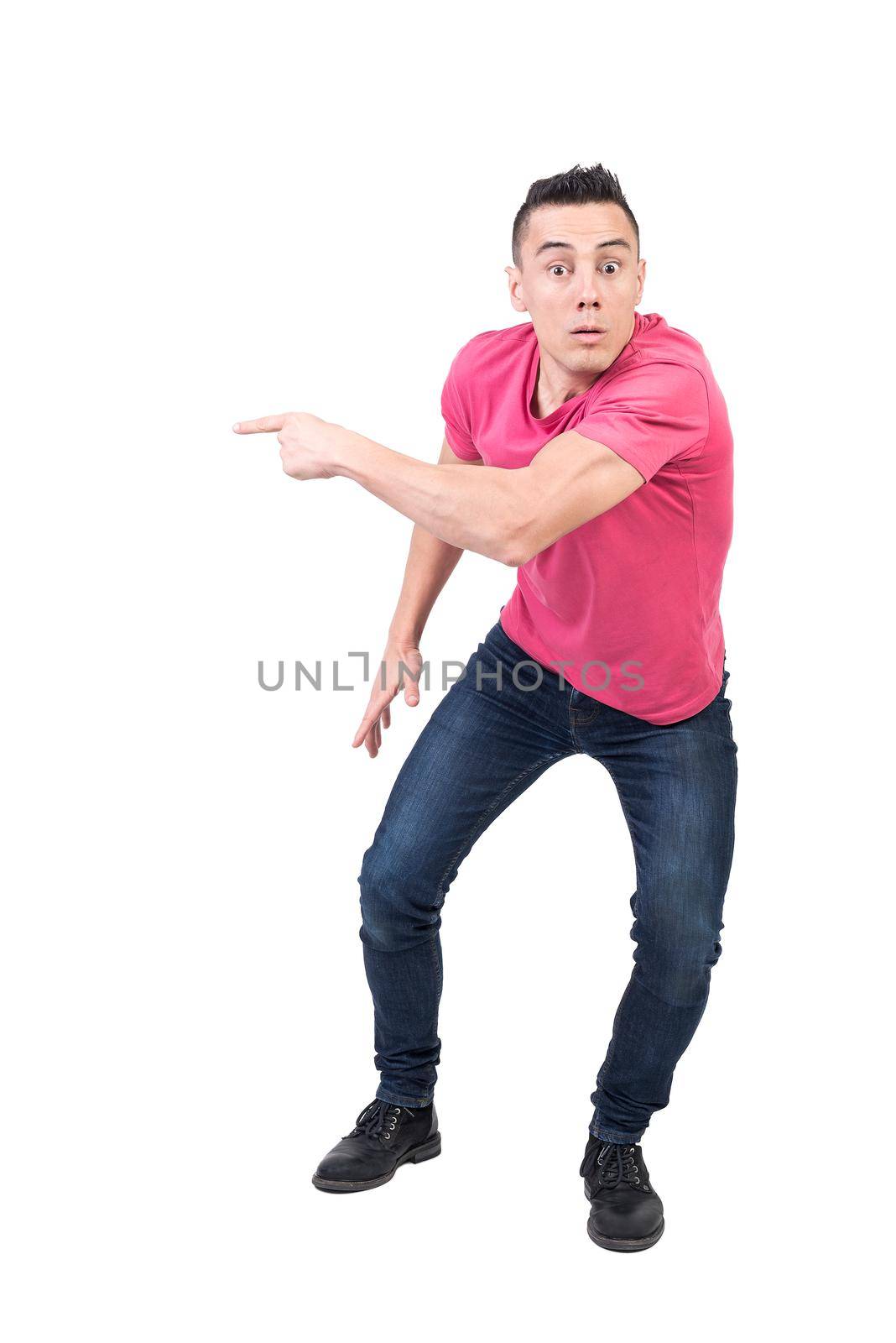 Full body of amazed male in casual clothes pointing aside and looking at camera with astonished face isolated on white background