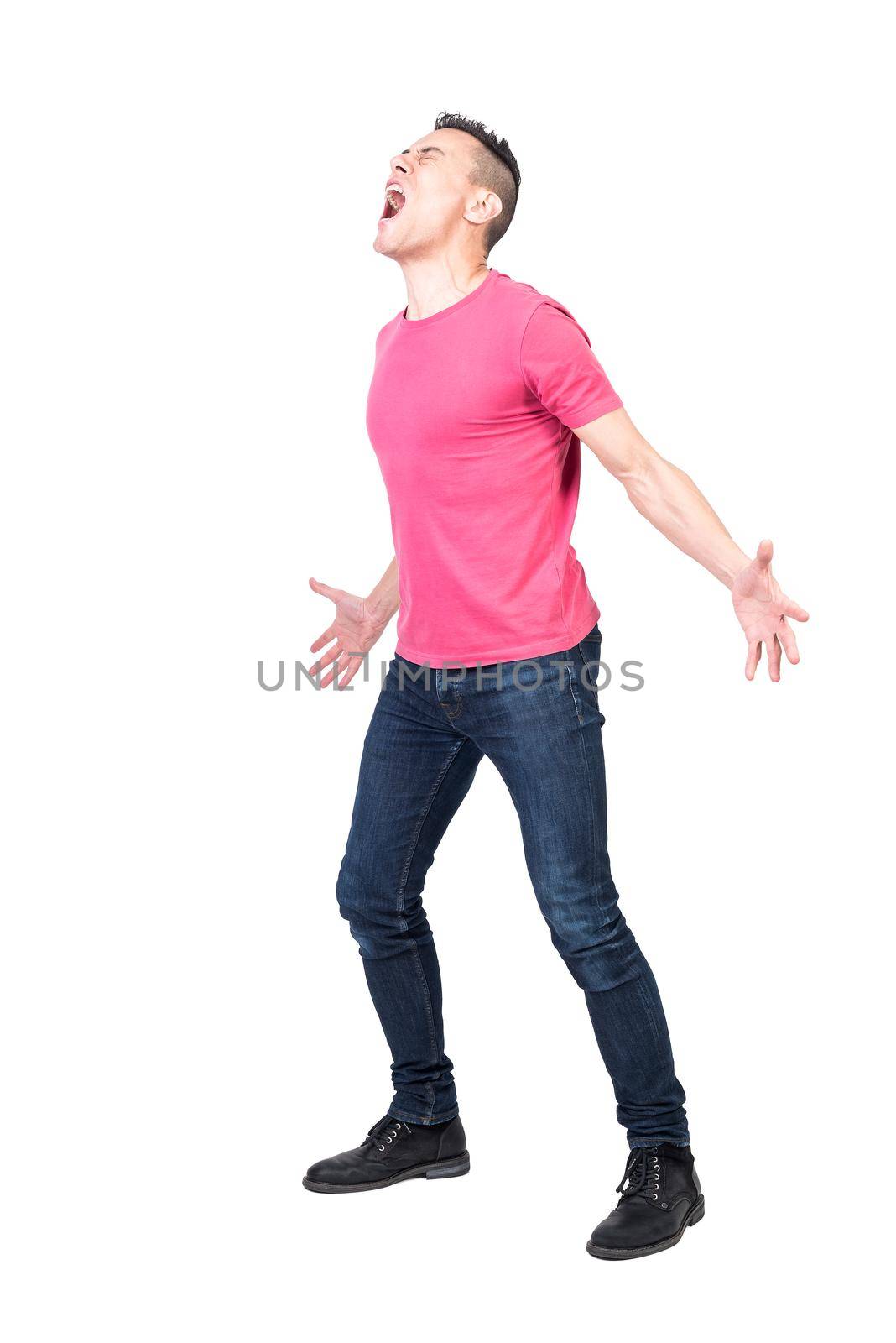 Full body of young annoyed man with dark hair in casual clothes screaming loudly with closed eyes and outstretched arms against white background