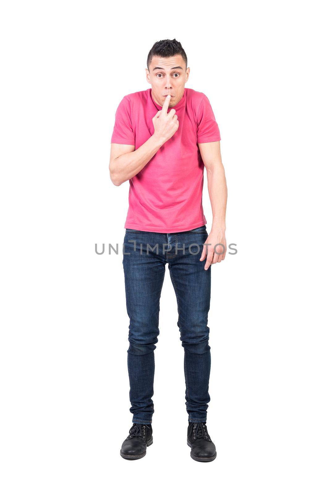 Full length ashamed male in jeans and pink t shirt touching lips and looking at camera while trying to hide his mistake against white background