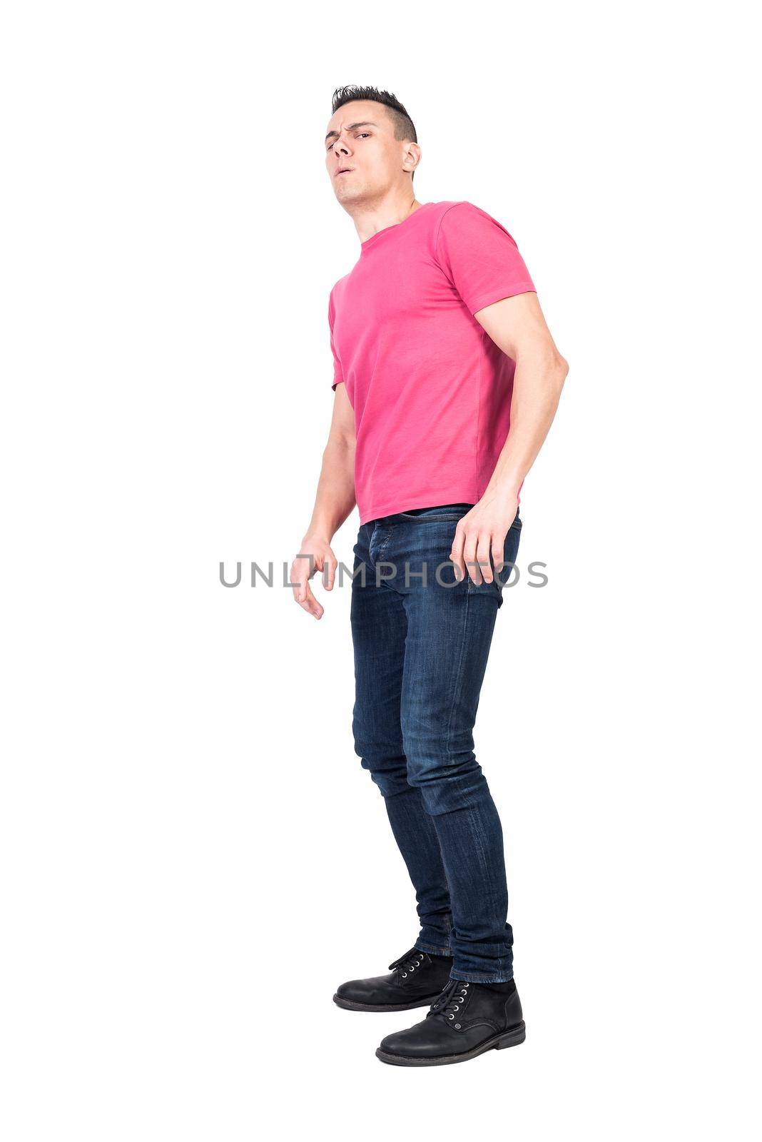 Full length man in jeans and pink t shirt tilting back and looking at camera with caution isolated on white background