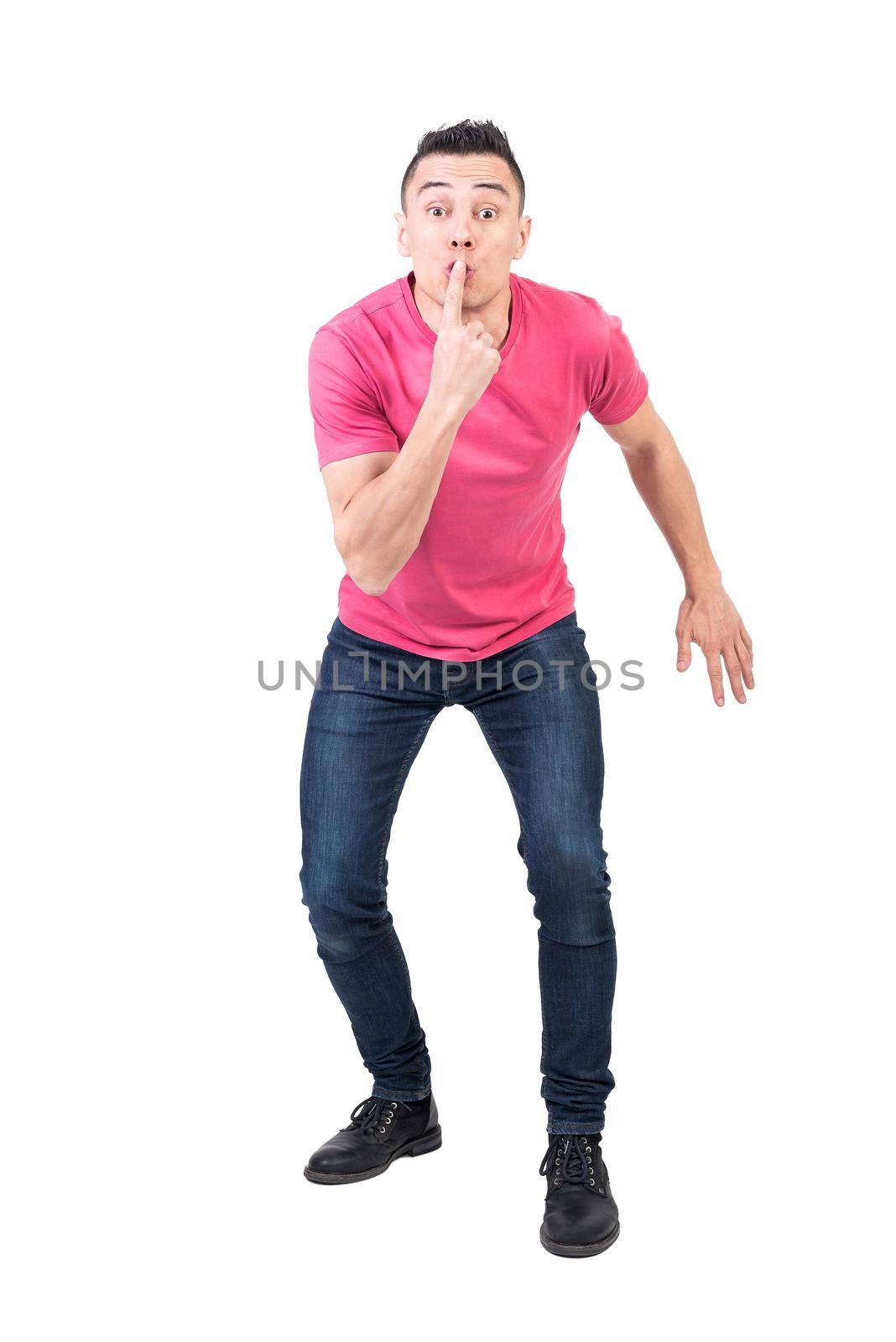 Full body of male model with eyes wide open asking to be quiet with finger on lips on white background