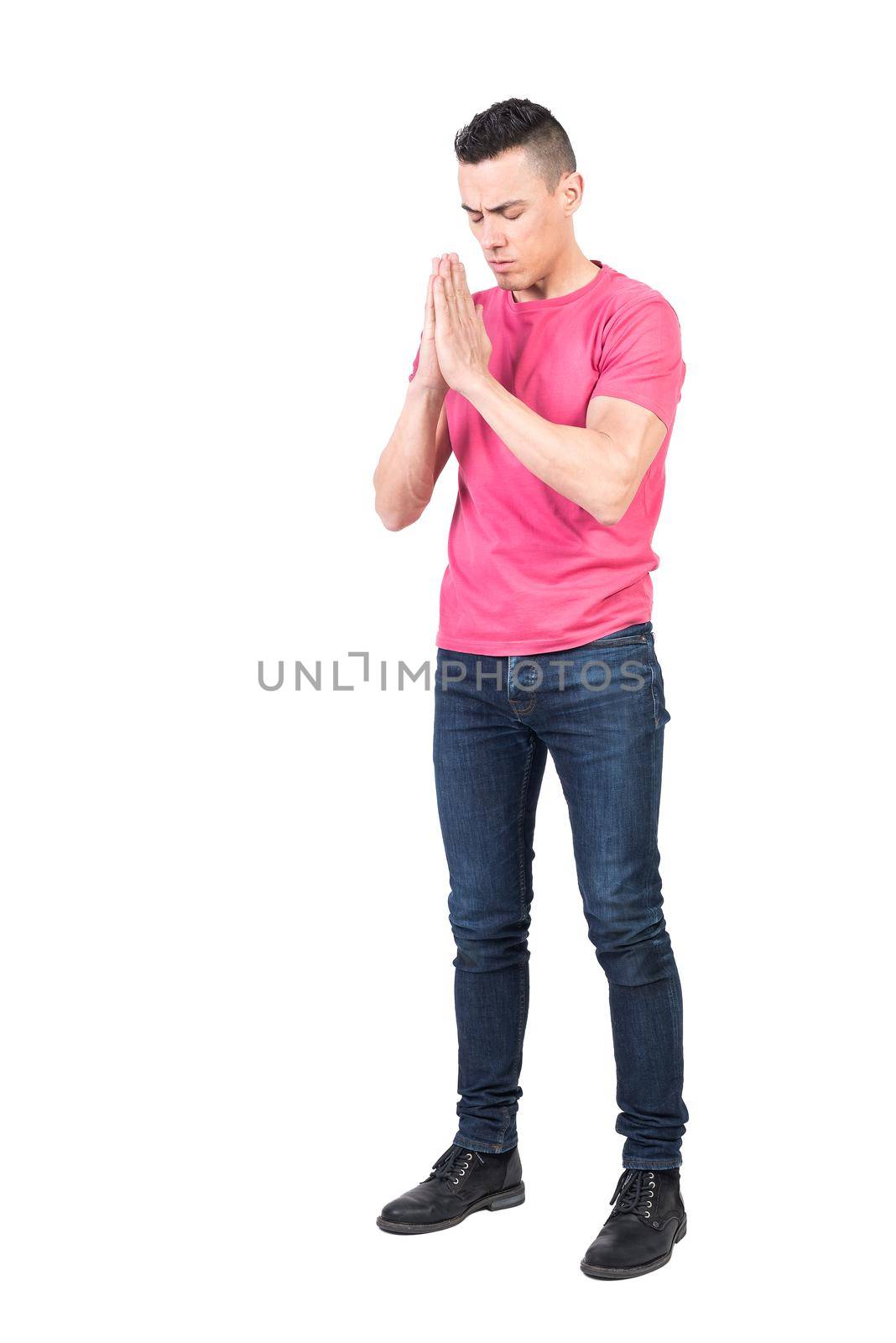 Full body of serene male in casual wear praying with closed eyes on white background