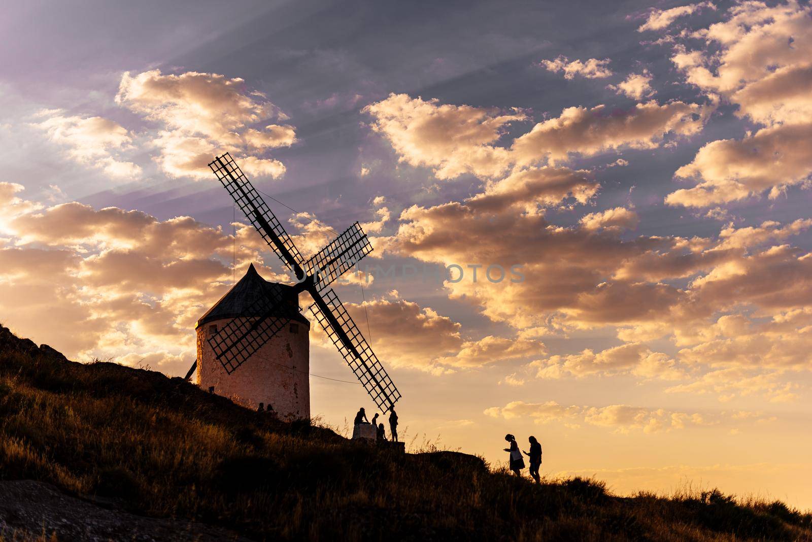 Photo with coopy space of people walking around an ancient windmill in a hill during sunset in Consuegra, Spain