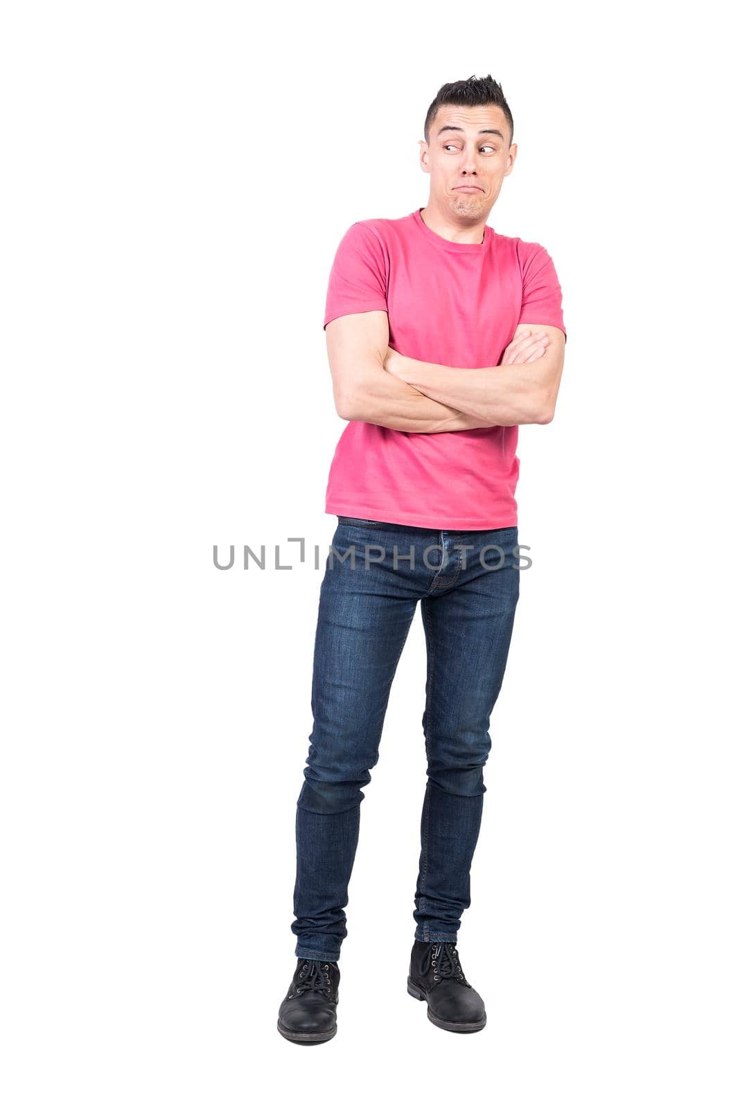 Full body of astonished male in casual clothes looking into distance while standing with crossed arms isolated on white background