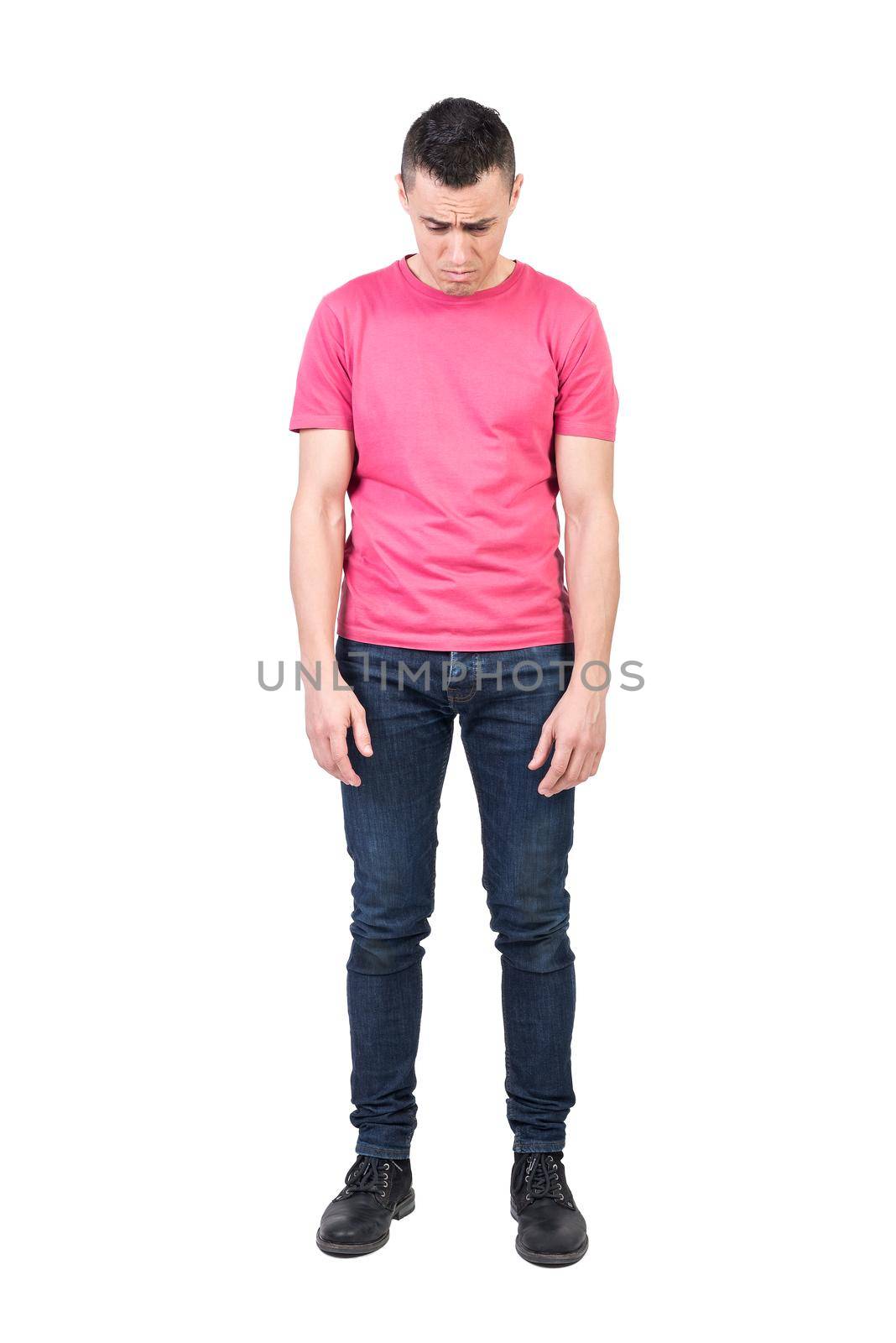 Full body of unpleasant young man in casual wear looking down while standing isolated on white background in light studio