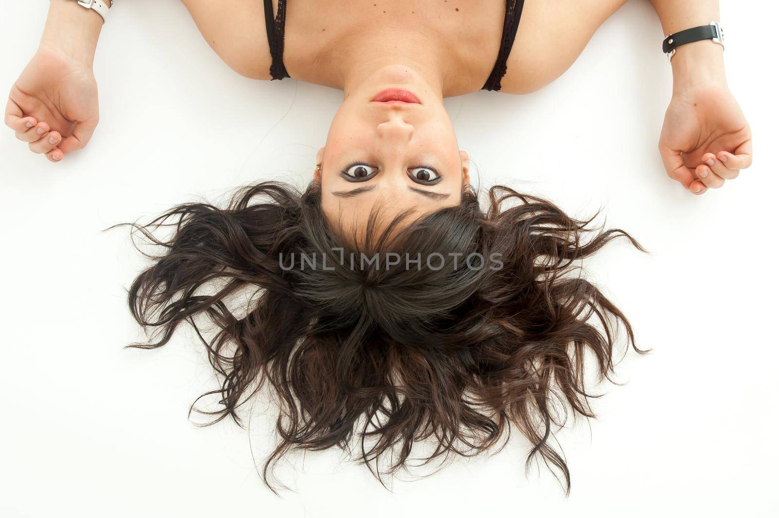 View from above of pretty brunette girl with long hair scattered on the floor staring at camera, on white background, close up