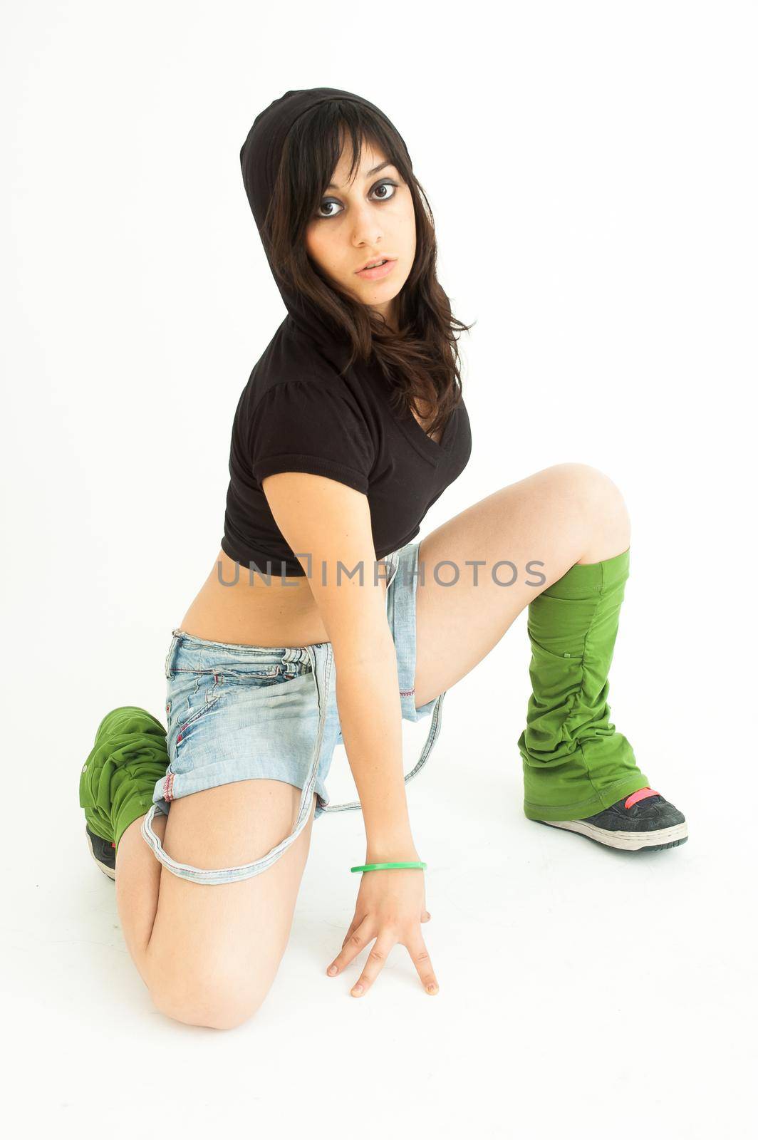 Modern pretty brunette girl on knees with shirt, short jeans staring at camera, on white background, long shot