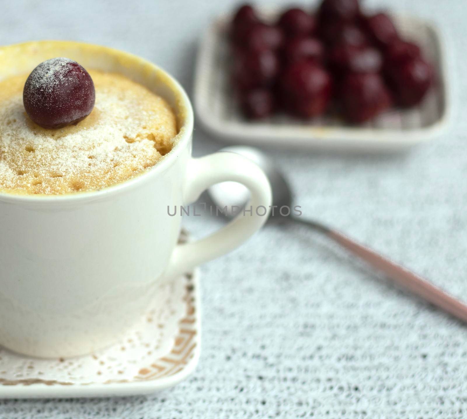 vanilla cupcake with cherries in a mug. Easy microwave cooking concept. The muffin is decorated with fresh cherries. White cup on a light background. Delicious sweet dessert. High quality photo