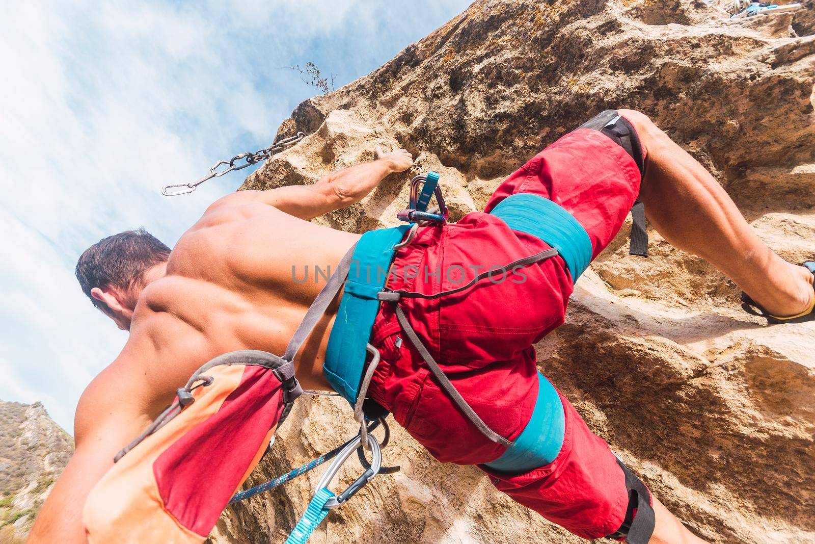 Close-up view from below of the back of a man climbing a rock.. Man with bare torso seen from behind climbing a rock formation.