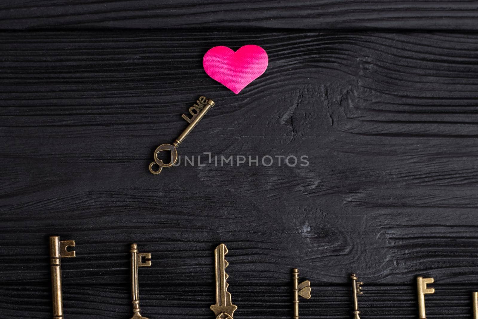 set of antique copper keys. small key with the inscription love, lies on a black wooden background near a pink heart. Heart keys concept, key selection. High quality photo
