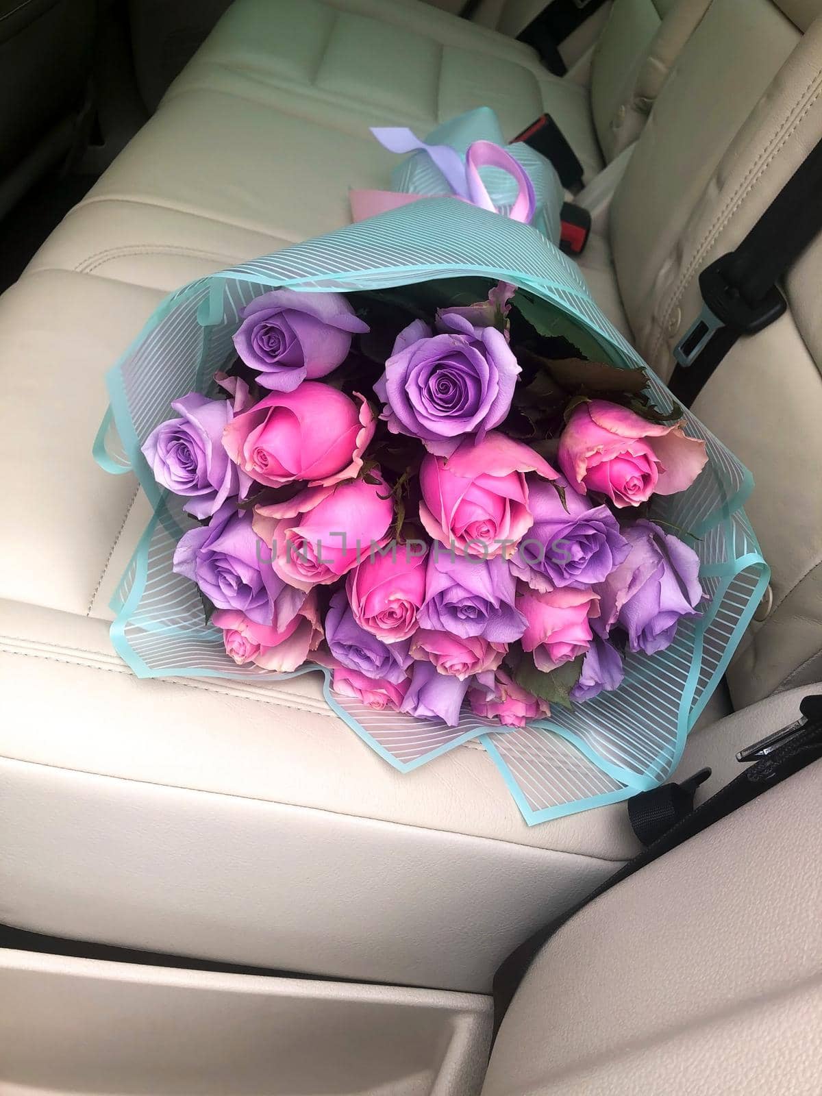 a bouquet of flowers lies on the light leather back seat of the car. Many lilac and pink roses are collected in a bouquet. Flowers wrapped in gift paper. Gift concept for girlfriend.