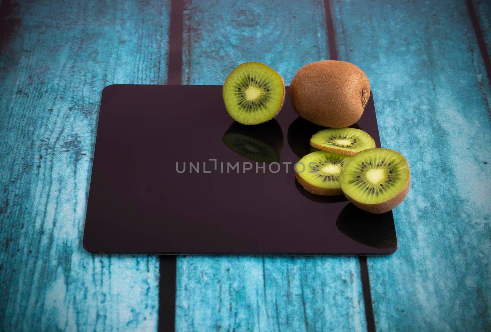 Fresh kiwi, whole and sliced, lie on a glossy black board. Place for text in the frame. High quality photo