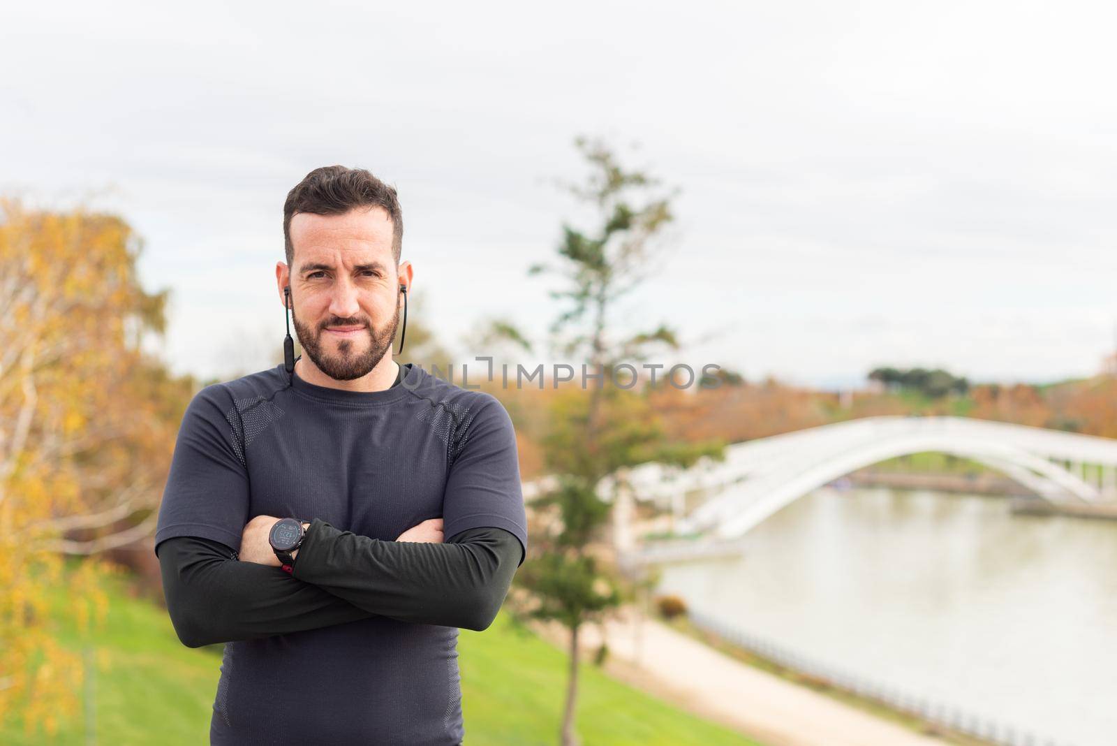 Caucasian sportsman with headphones is standing with crossed arms . High quality photo