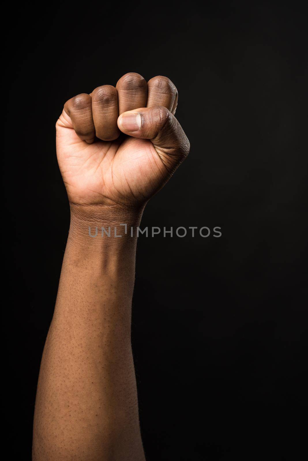 Raised fist of a black man, in a fighting attitude. on black background.