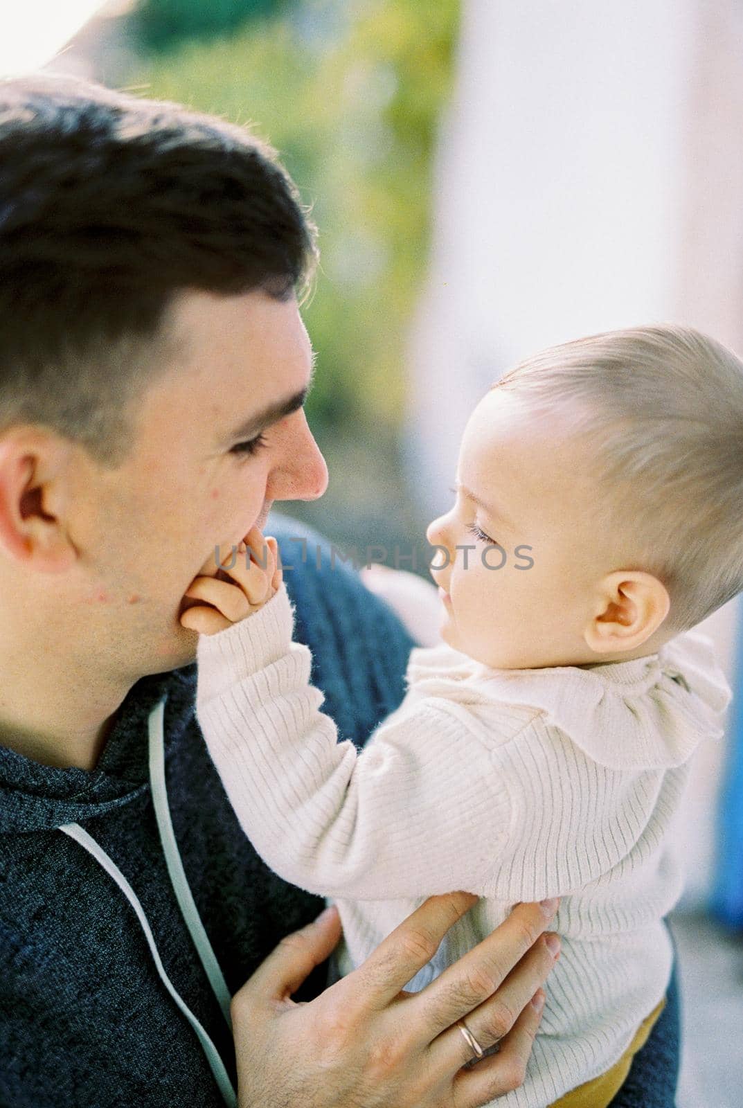 Baby touches his father face with his fingers, sitting in his arms. Portrait by Nadtochiy