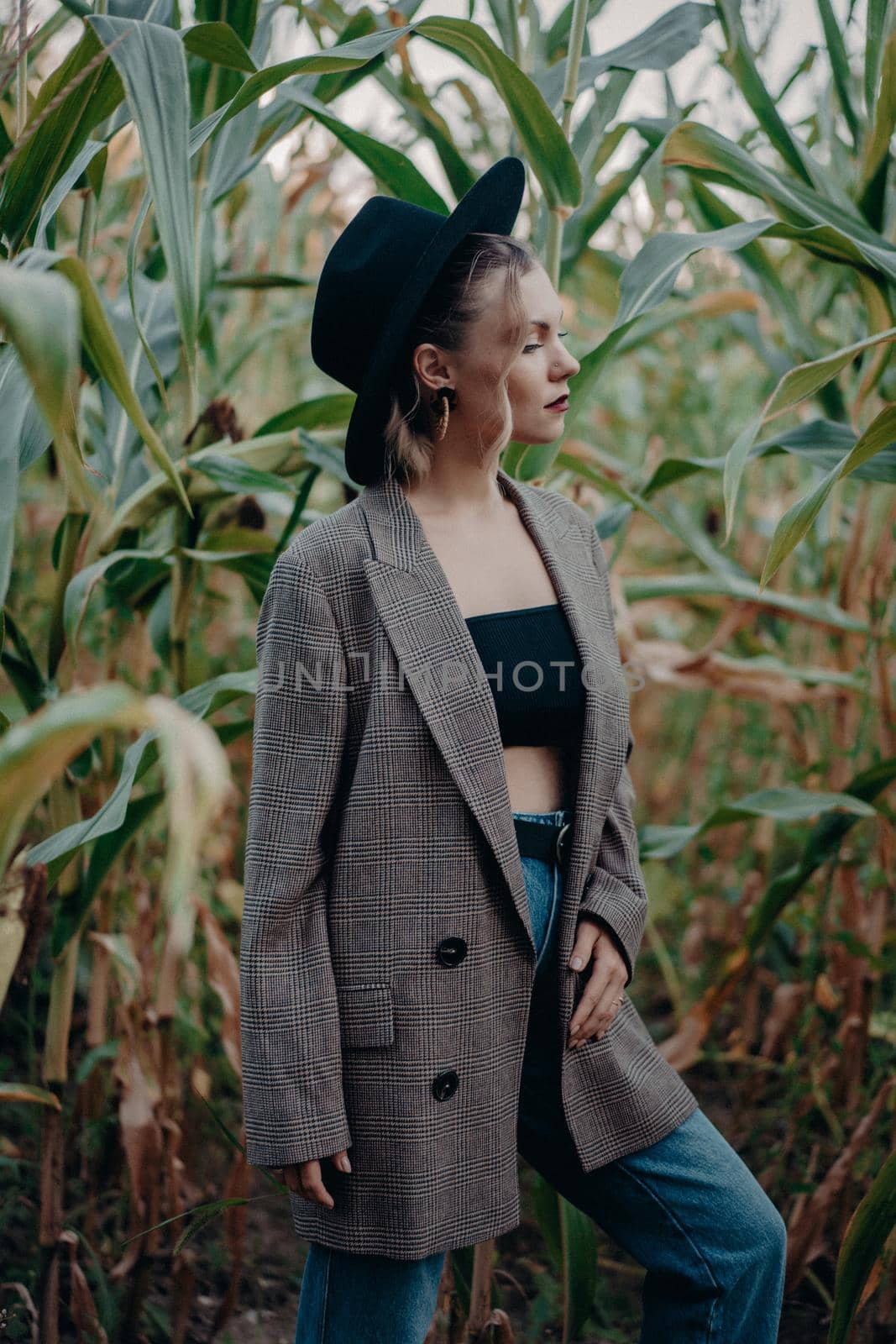 Trendy woman in plaid blazer and hipster hat at corn background. Fashion girl portrait, she posing on natural landscape. High quality photo