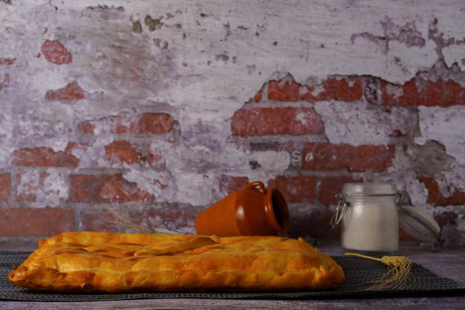 tuna pie with flour jar and earthenware jar in the background a red brick wall