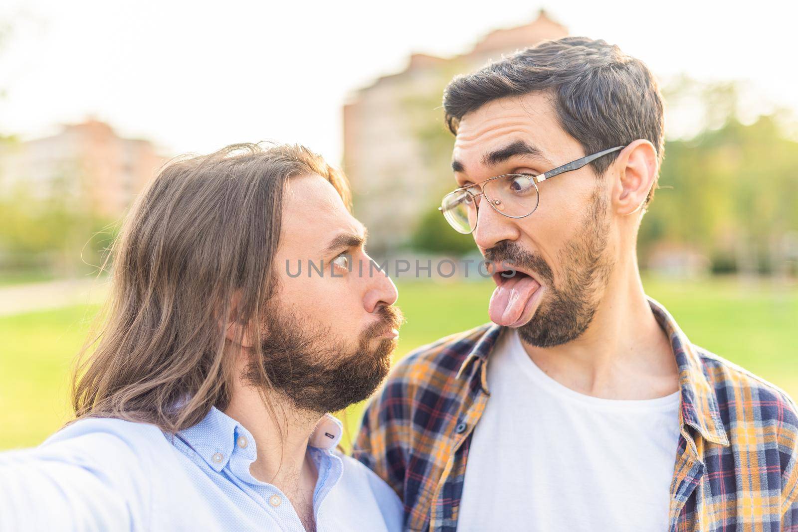 Front view of a funny gay couple looking at each other and making grimaces in the park.