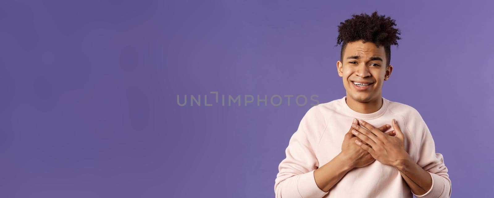 Close-up portrait of handsome silly hispanic guy with dreads, place hands on heart and sighing as contemplate something adorable speaking from all his soul, thanking for praises, purple background.