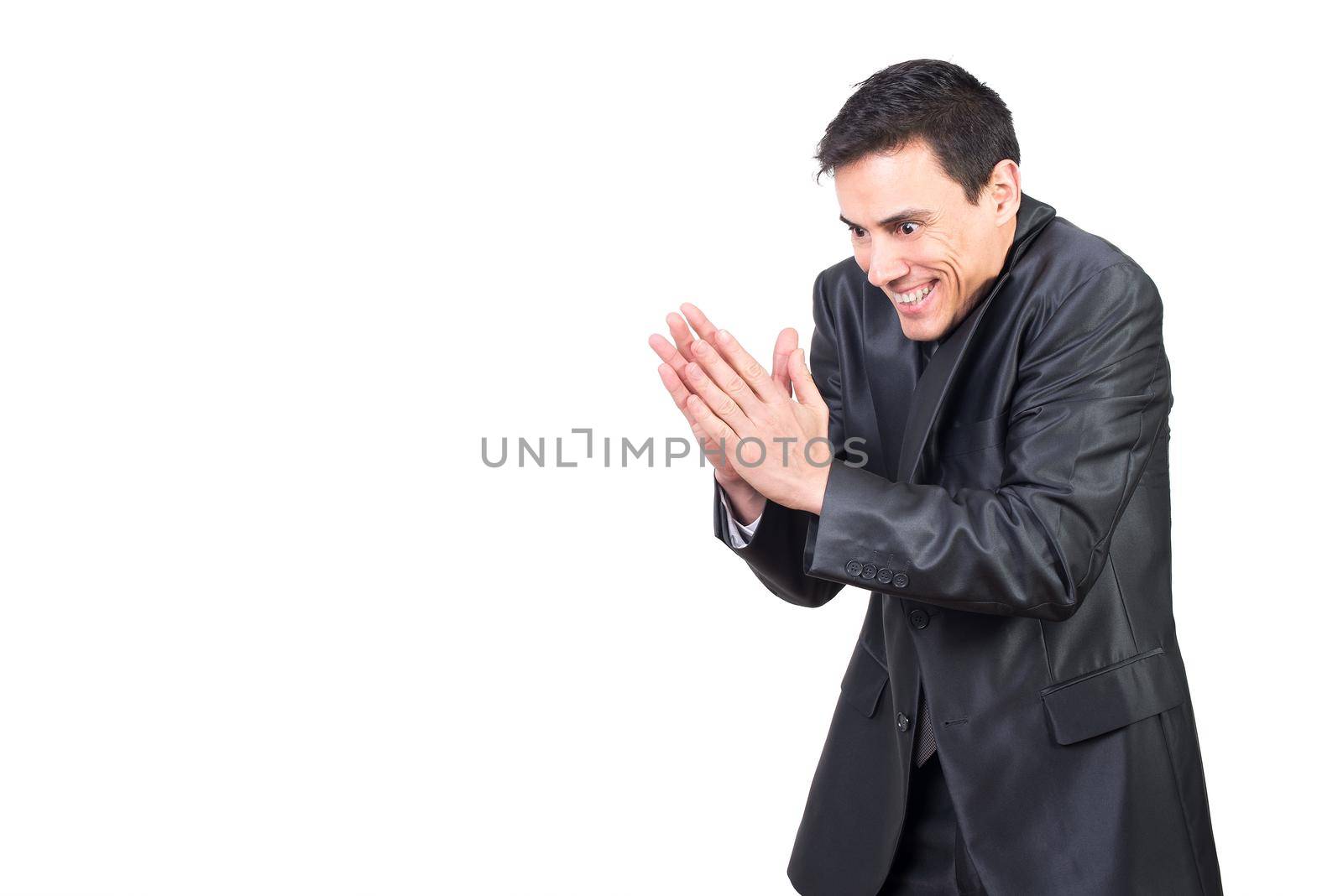 Vicious male with black hair in formal suit rubbing hands with evil face while standing isolated on white background in light studio