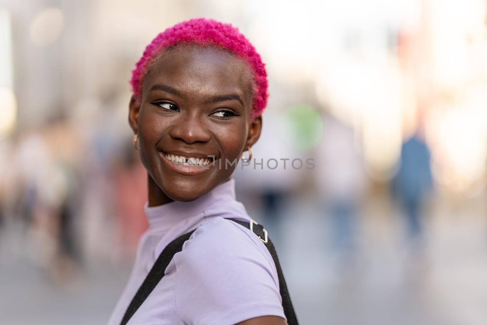 Portrait of a young african woman with short pink hair turning and smiling in a city