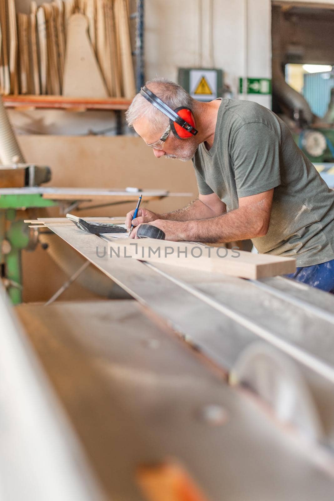 Worker noting measurements of wooden step on a sliding table saw, vertical background