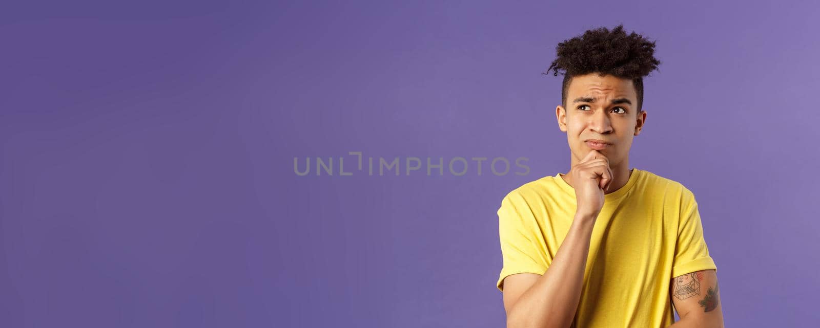 Close-up portrait of indecisive, puzzled attractive young man have problems, lacking idea, thinking, look away frowning and grimacing troubled, standing thoughtful purple background.