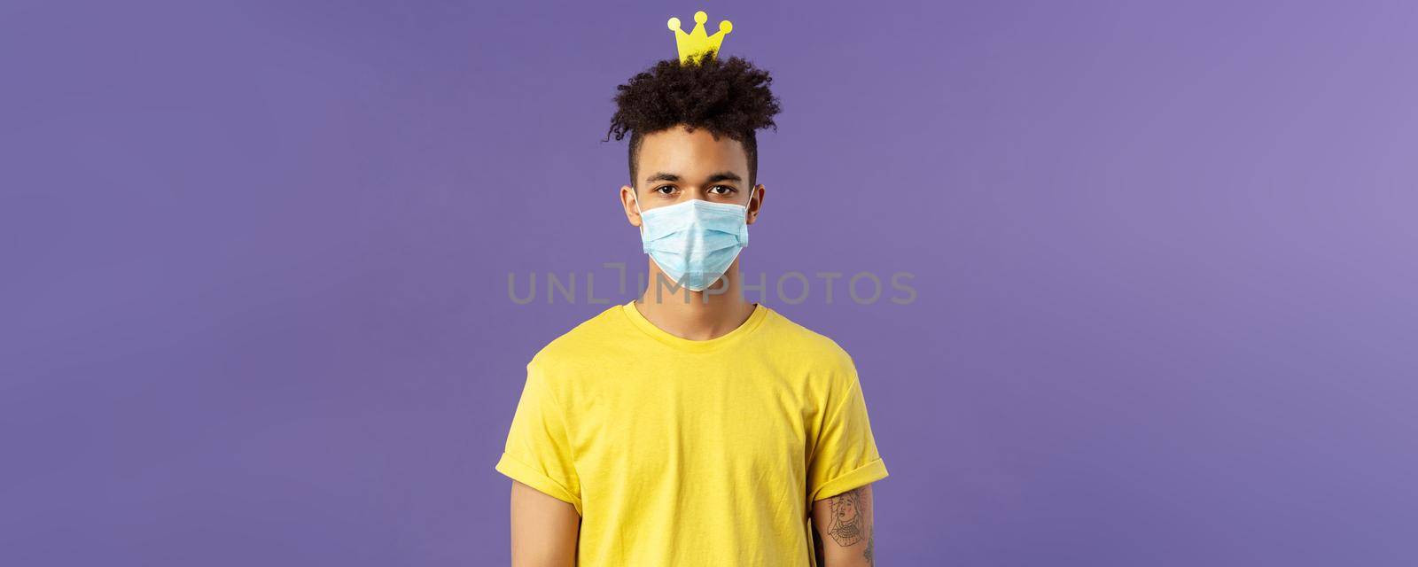 Portrait of funny hispanic guy in face mask, fool around, going crazy staying inside home during quarantine, wearing small crown and look camera, social-distancing, staying healthy covid19 pandemia.