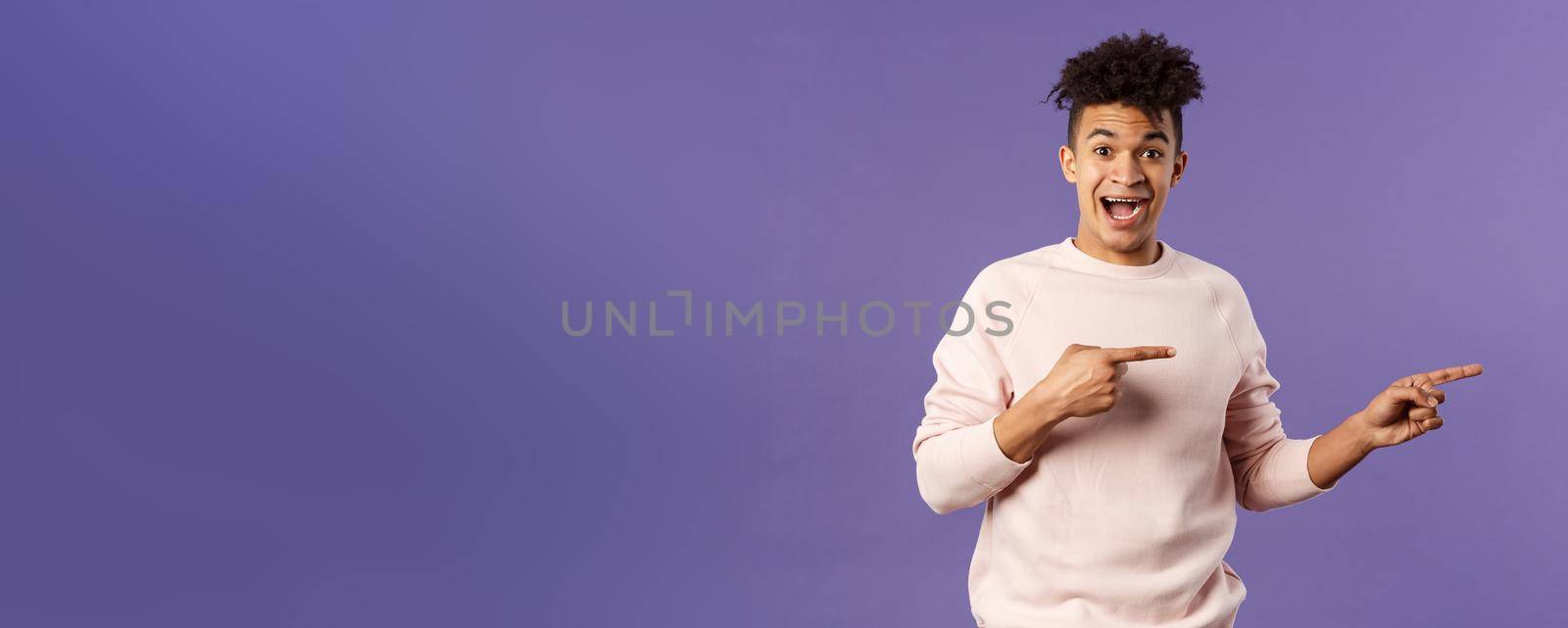 Portrait of enthusiastic lively hipster male 25s, pointing fingers right inviting join courses, sign up for awesome deal, best delivery service or online shop, look amused and happy camera by Benzoix