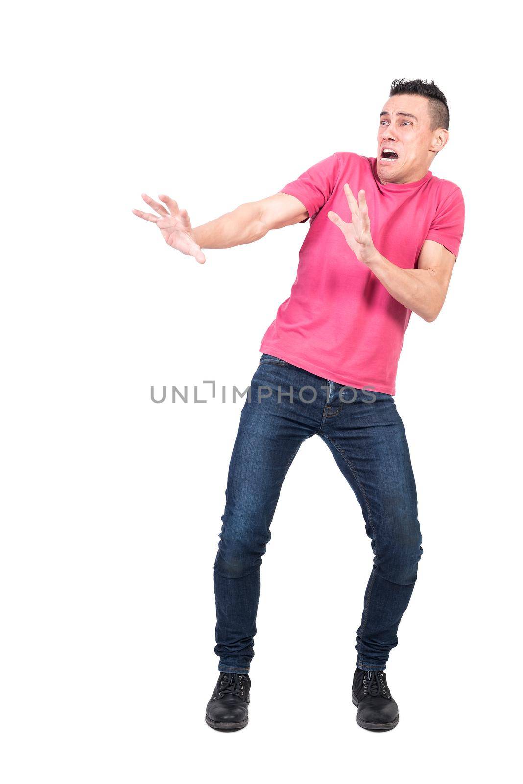 Full length terrified male in jeans and pink t shirt making protective gesture and looking away while yelling in horror against white background