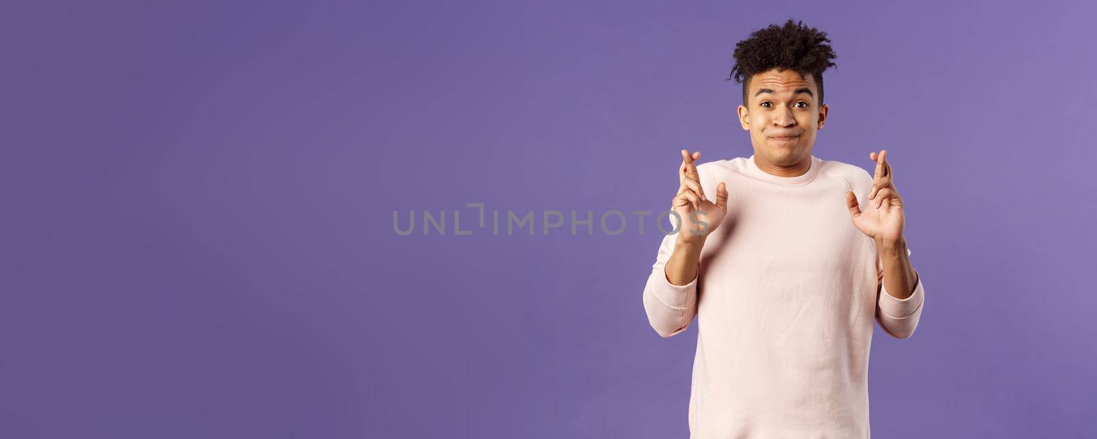 Portrait of young hopeful handsome man with dreads ancitipating something good happen, cross fingers good luck, smiling with joy and optimism, having faith, praying over purple background by Benzoix