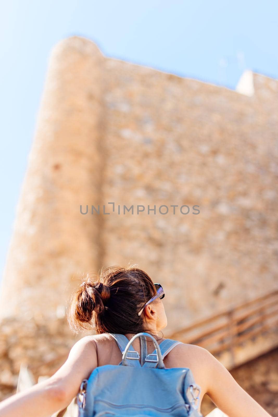 Vertical photo of a young woman with a backpack visiting and contemplating an historical castle in Consuegra, Toledo in Spain.