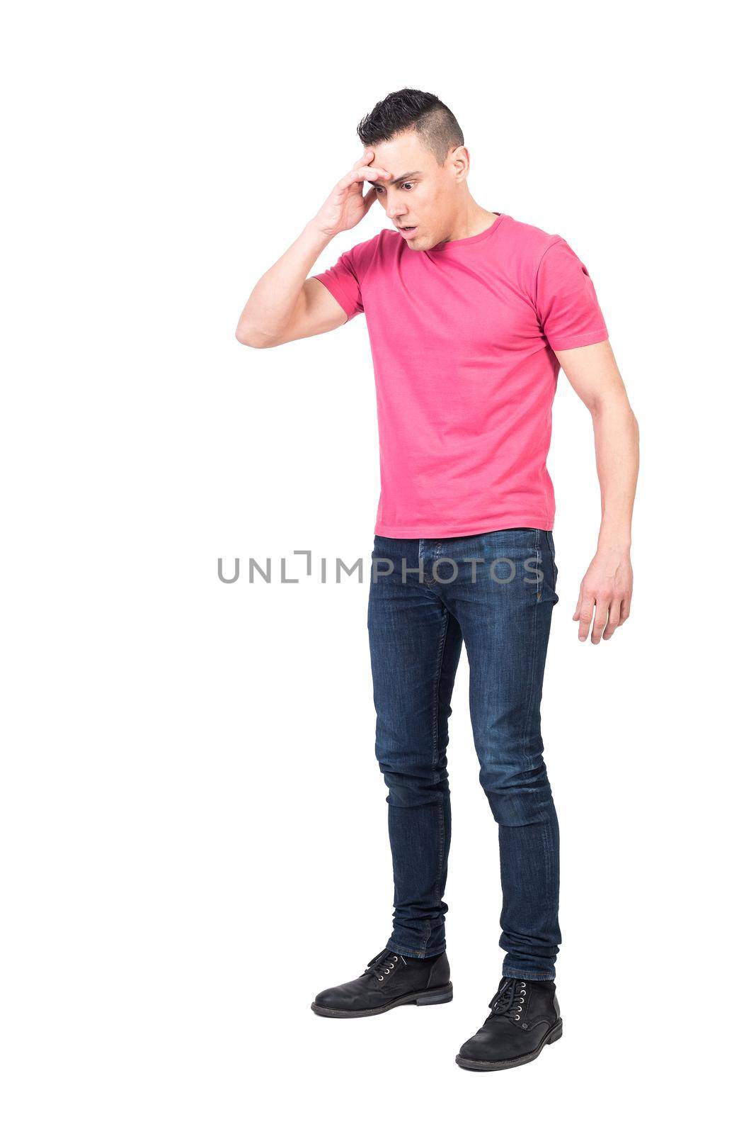 Full body of shocked young male with dark hair in casual outfit touching forehead and looking down with opened mouth against white background