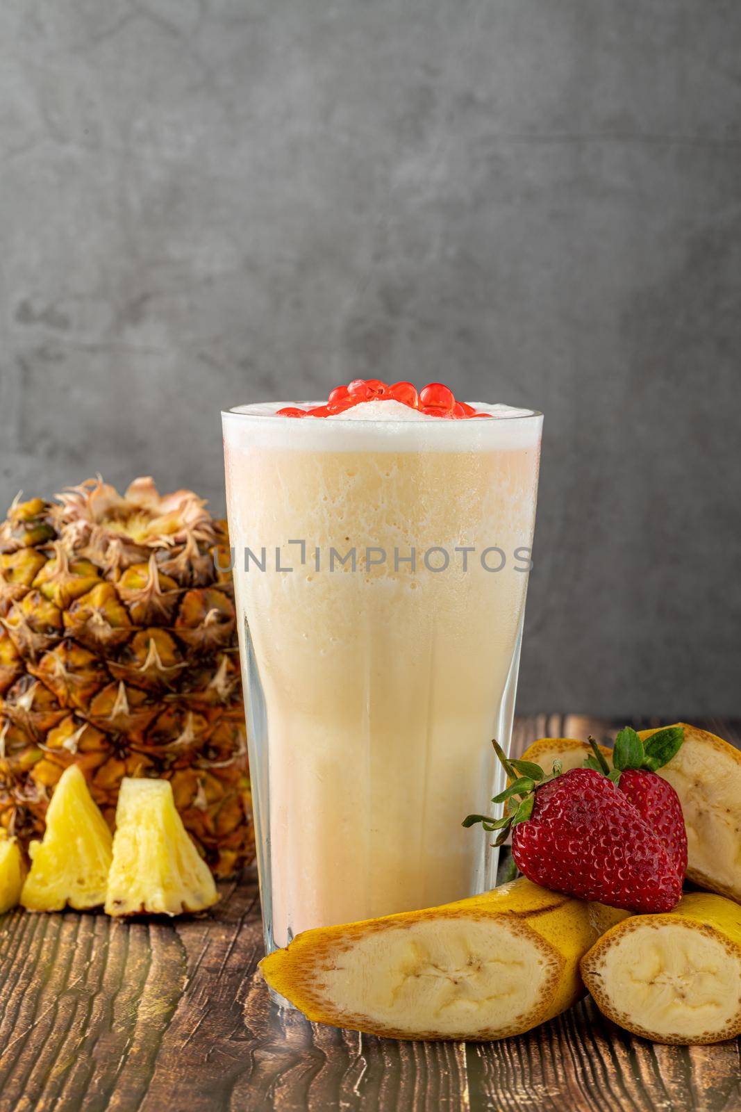 Banana, strawberry and pineapple smoothie on wooden table and bubble tea or boba tea balls on it by Sonat