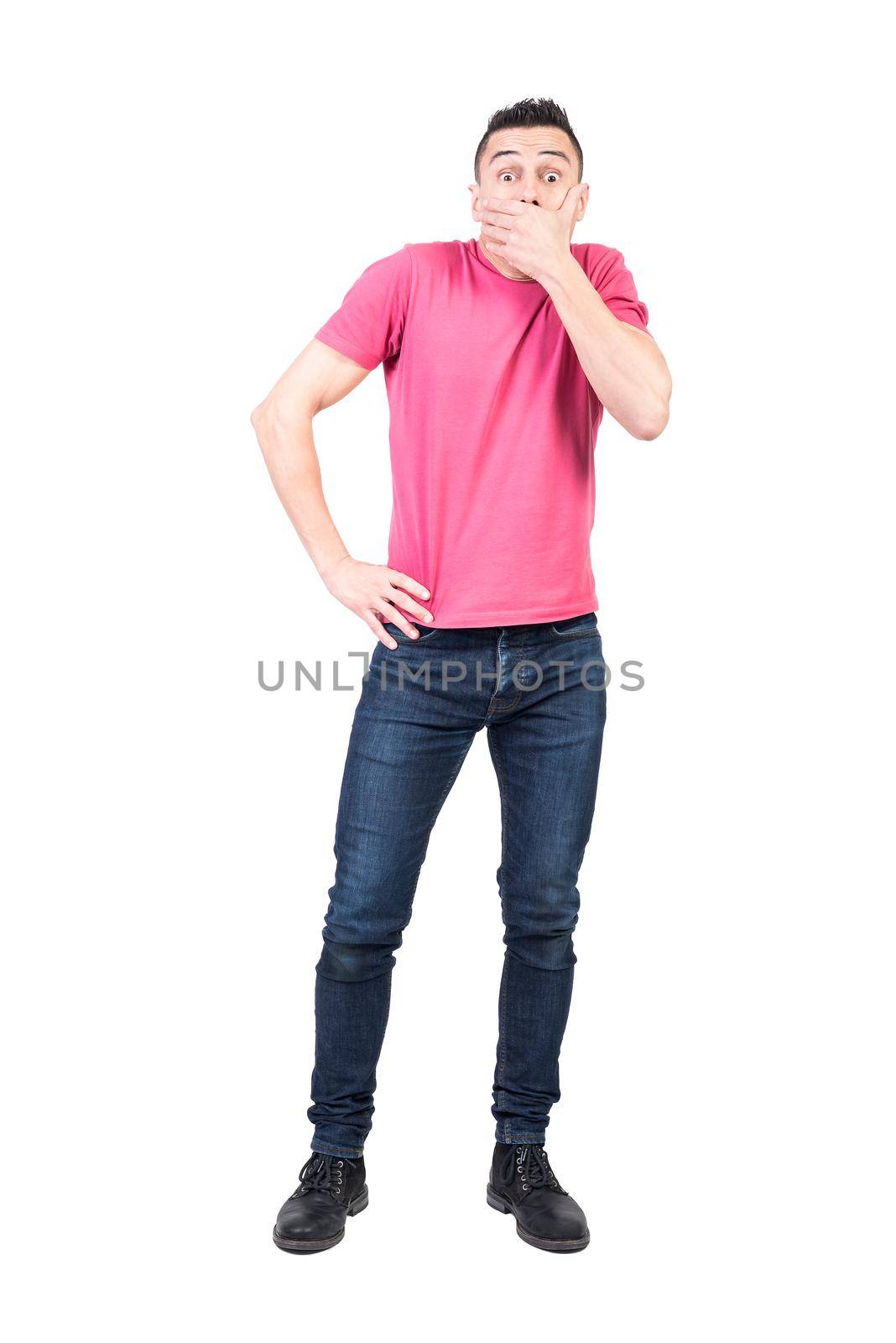 Full body of shocked male covering mouth with hand and looking at camera while standing with hand on waist isolated on white background