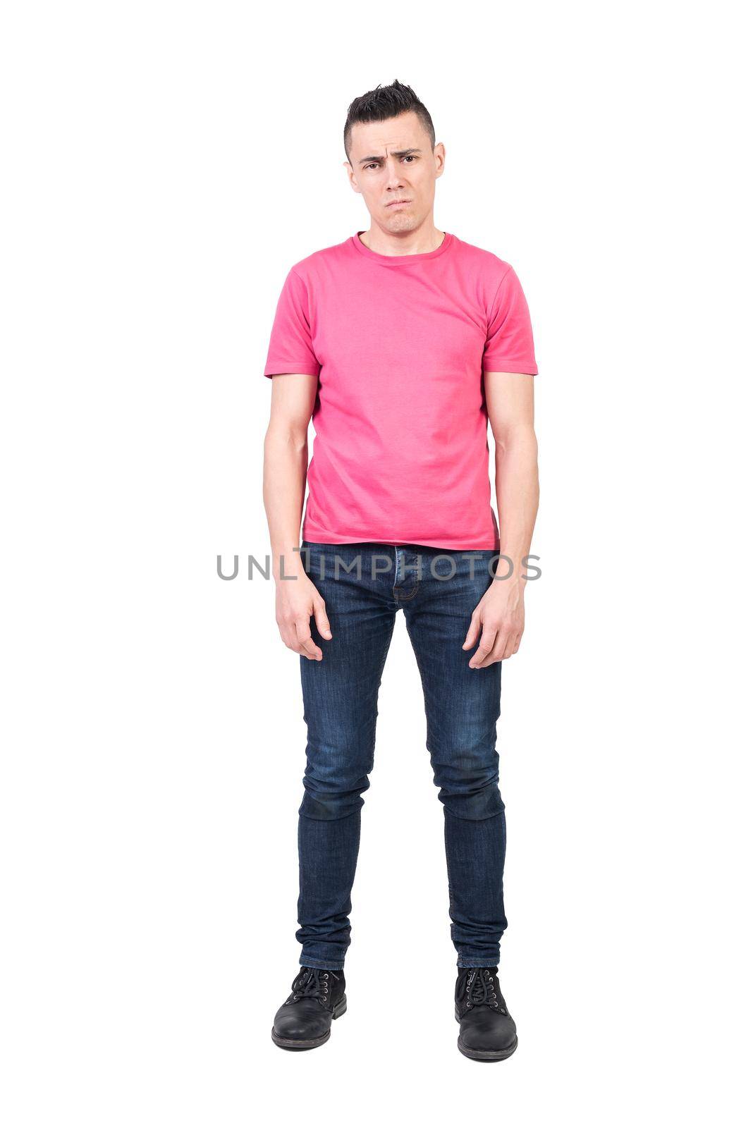 Full body of unhappy man looking at camera with discontent face impression while standing isolated on white background in light studio