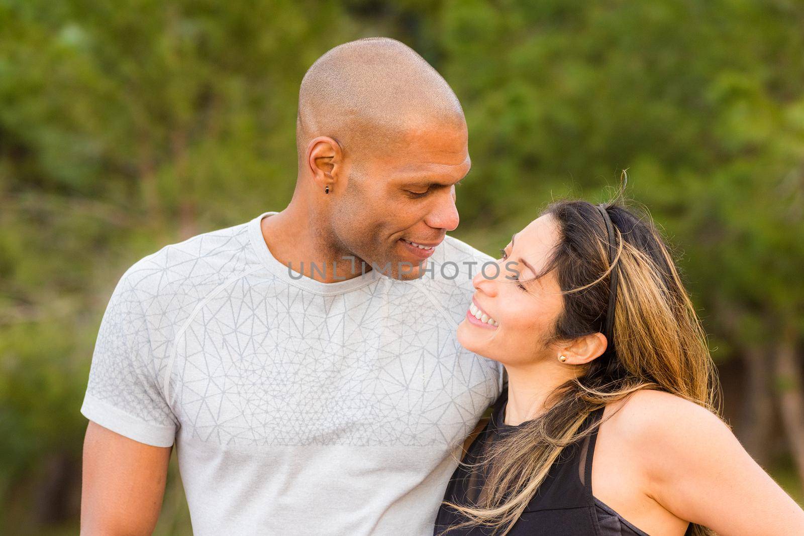 Portrait of fitness couple hugging and looking at each other. Multi-ethnic couple exercising outdoors.