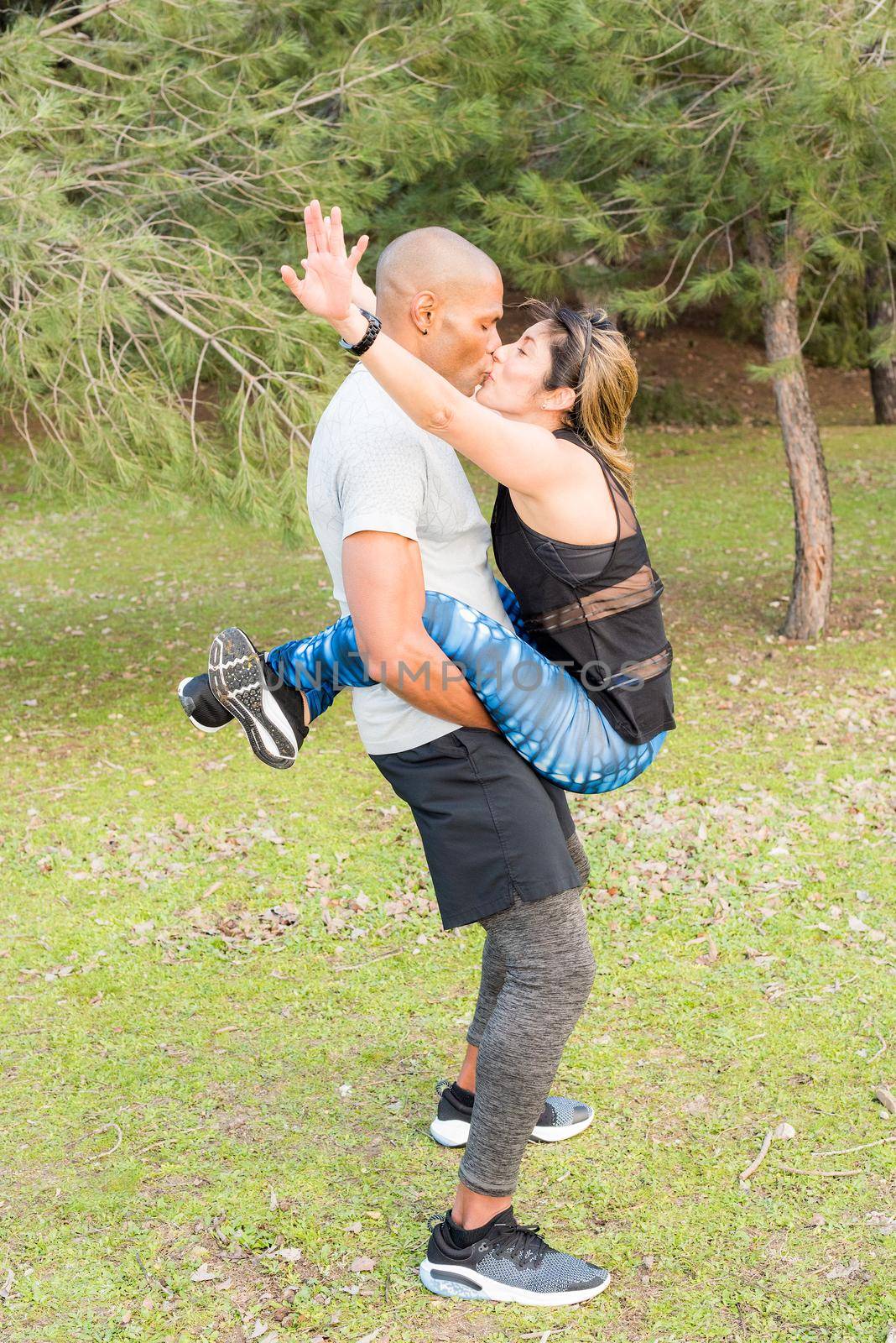 Fitness couple doing abdominal excersise while he holding she for her legs and kissing each other. Couple doing exercise outdoors together.
