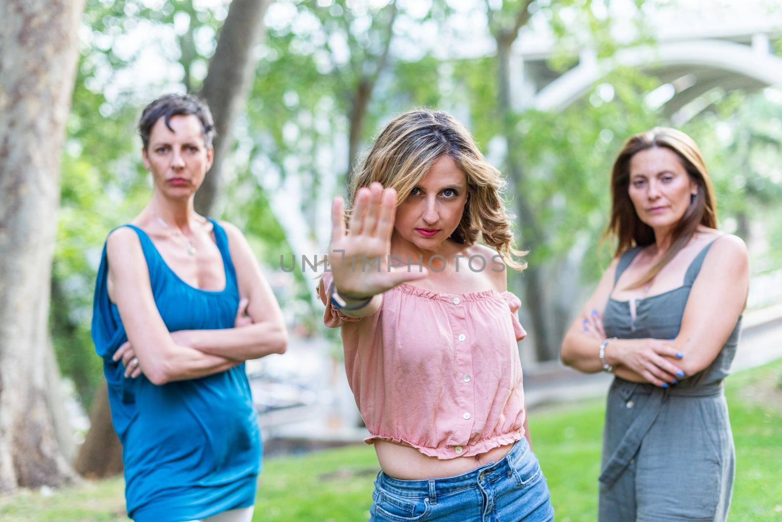 A mature adult woman making the stop gesture with a serious expression. Two women on each side with their arms crossed.