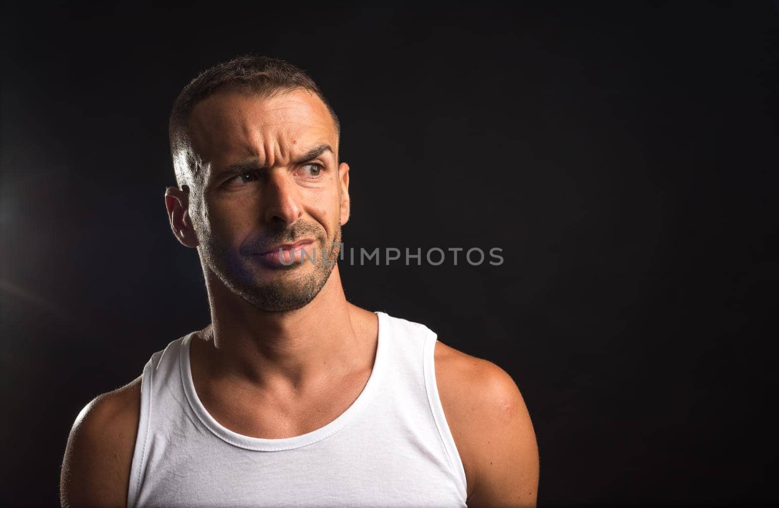 Distrustful athlete man in tank top. Close up. Black background.