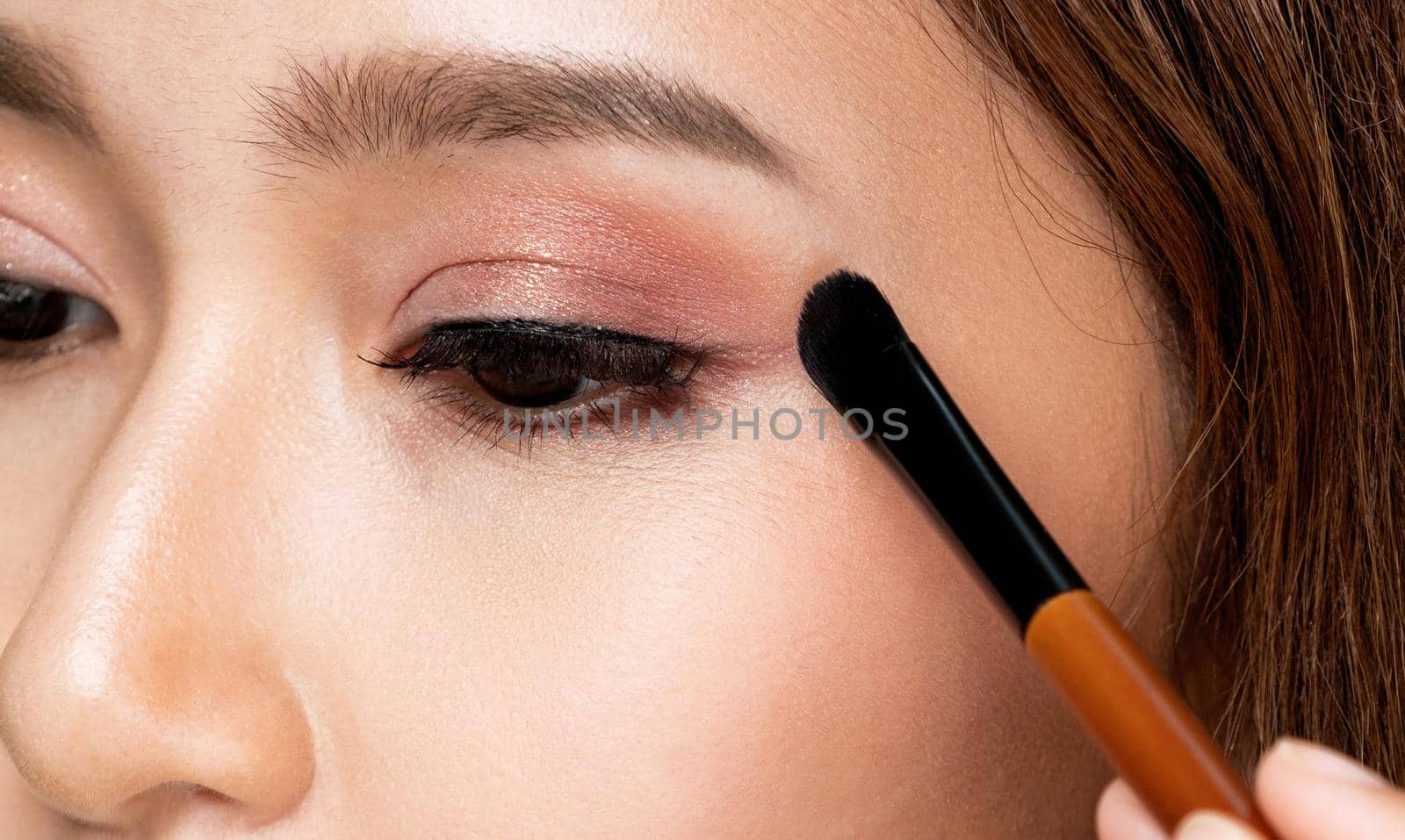 Closeup ardent female model applying her eyeshadow and holding a mirror. by biancoblue