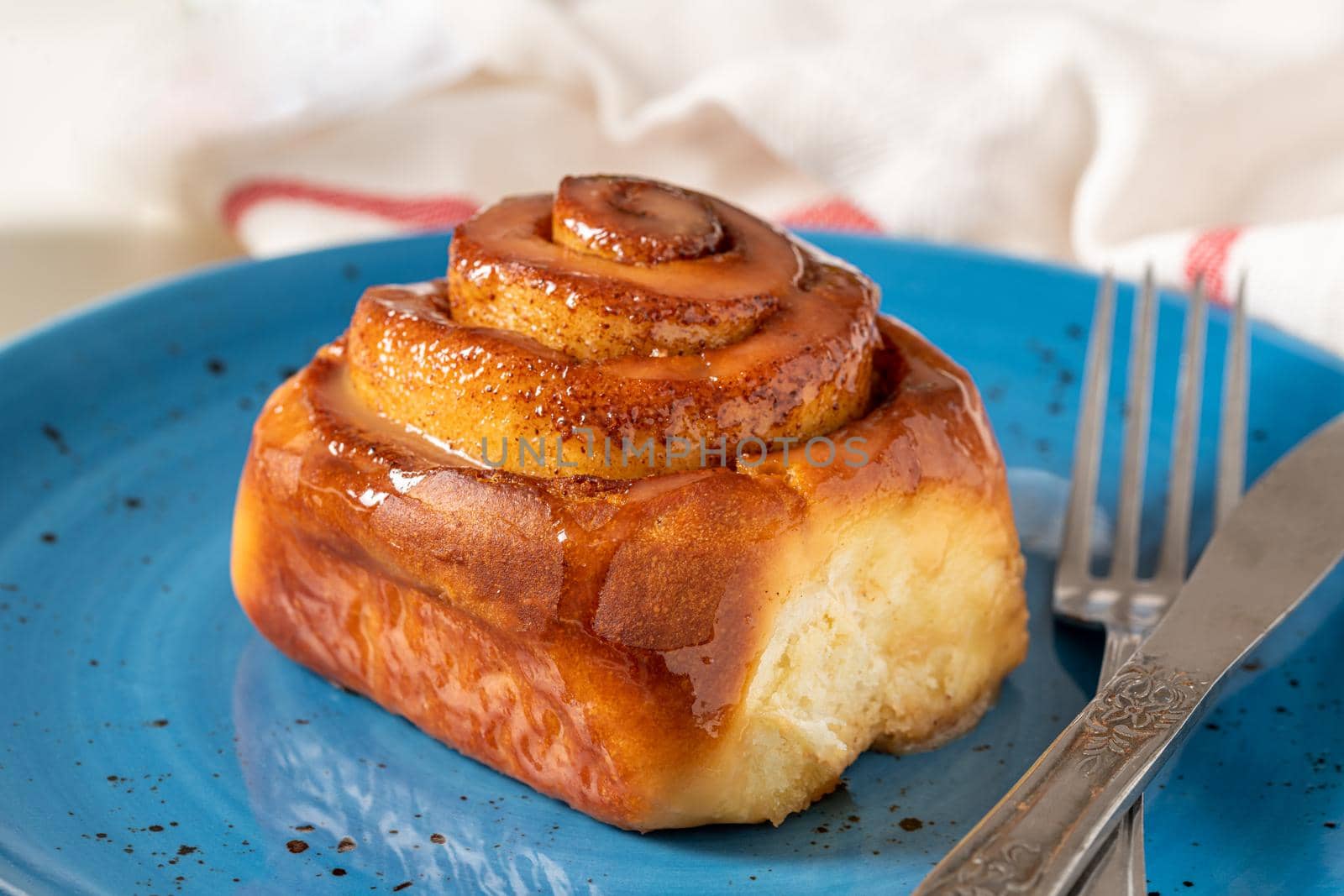 Freshly baked cinnamon roll on a blue porcelain plate by Sonat