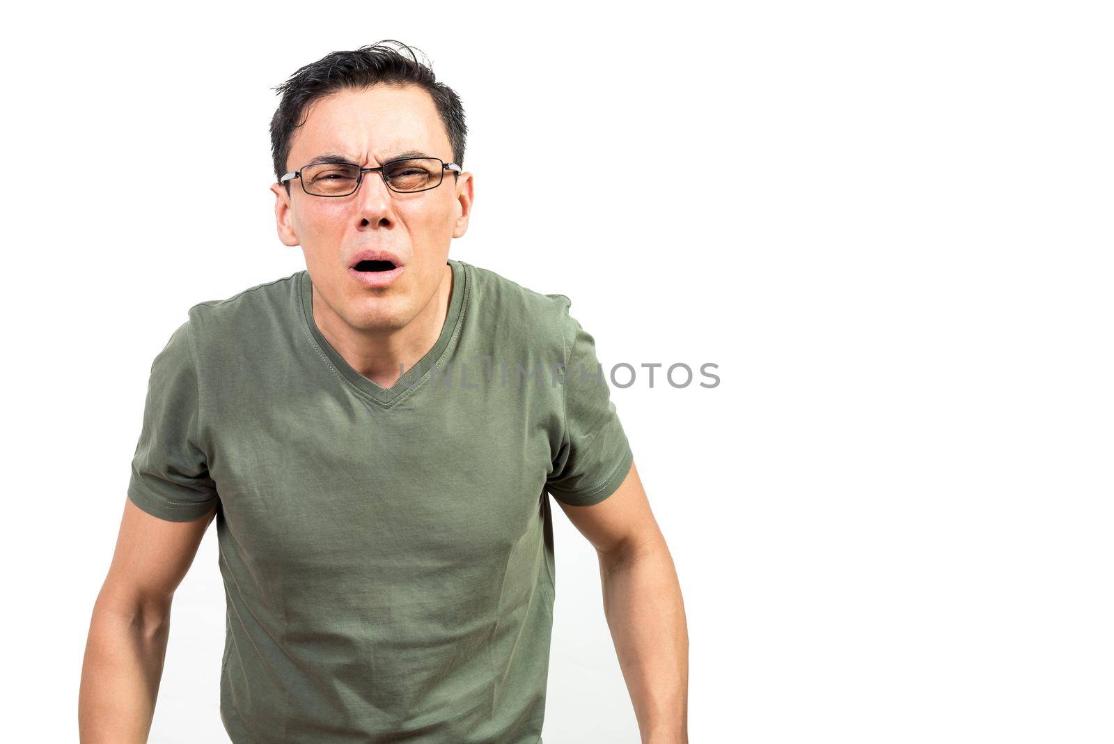 Blind nerdy man in green t shirt and glasses squinting and looking at camera against white background