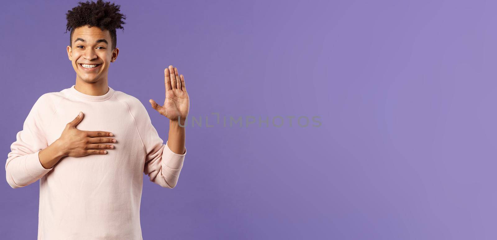 Portrait of young happy, joyful hispanic man making honest statement, promise to tell only truth, hold one hand on heart and another raised, smiling sincere, standing purple background.